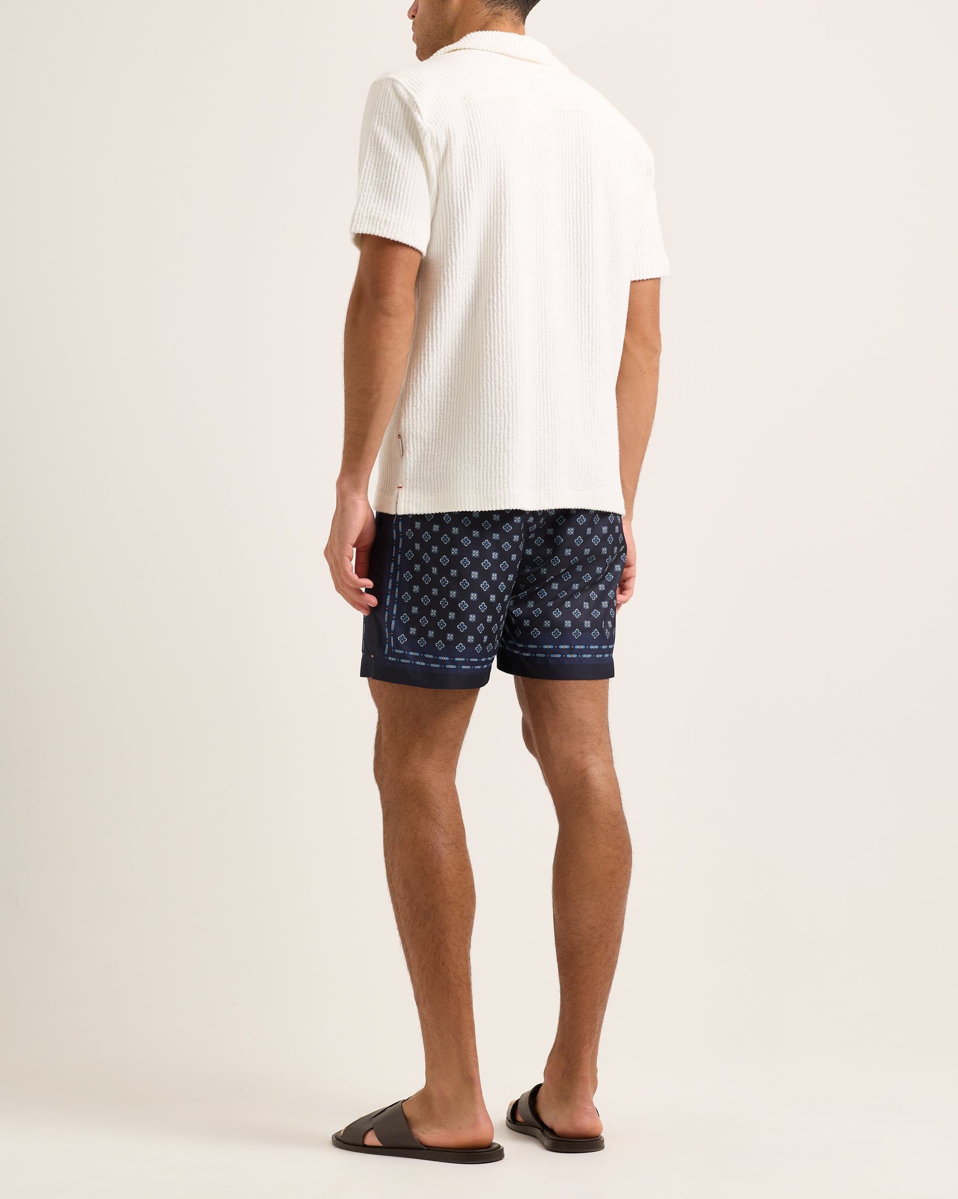 Model wearing a white textured shirt with swim shorts on a plain background