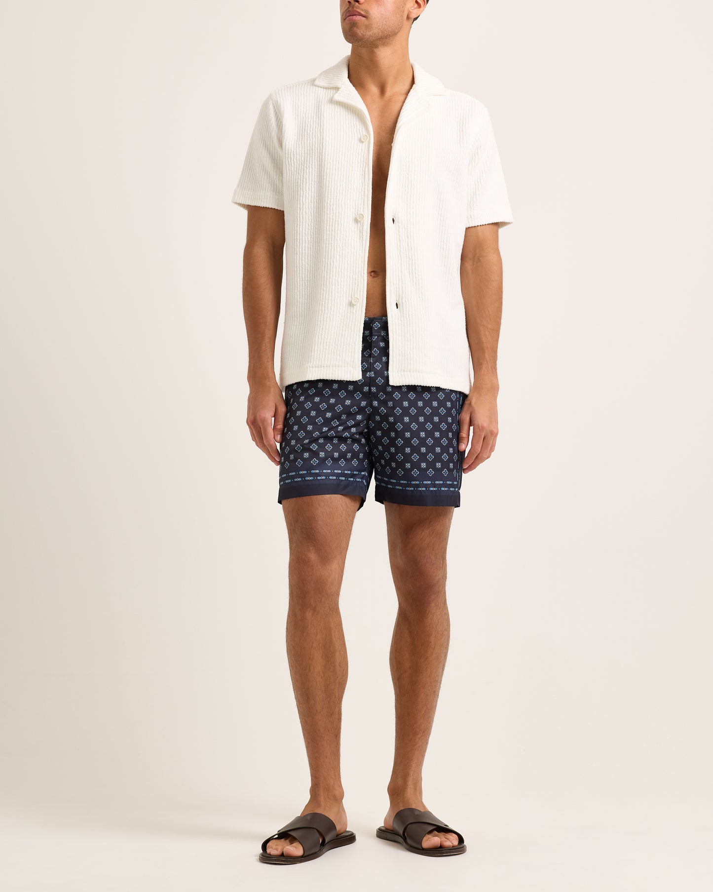 Model wearing a white textured shirt with swim shorts on a plain background