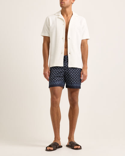 Model wearing a white textured shirt with swim shorts on a plain background