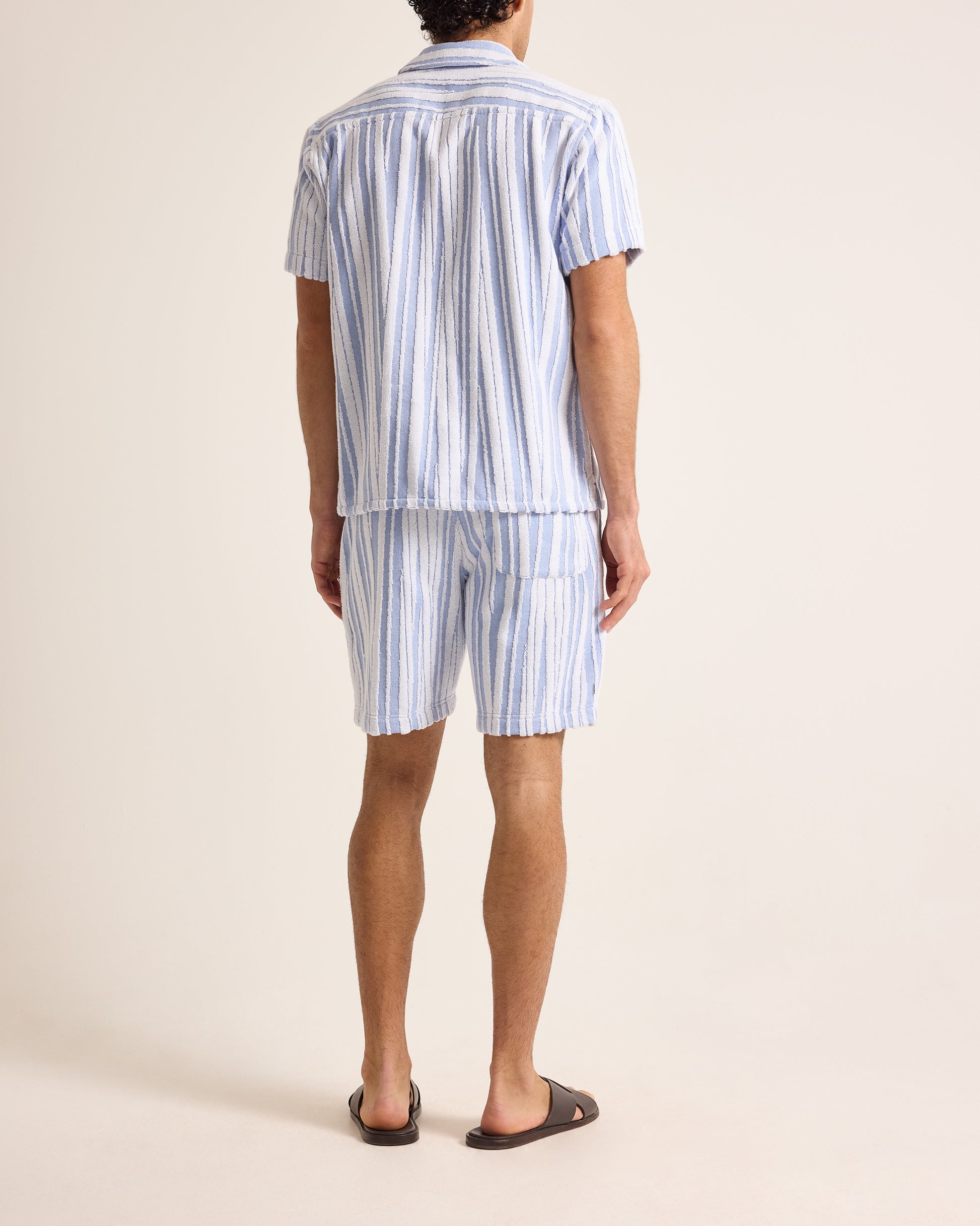 Person wearing a blue and white striped shirt and shorts set on a beige background