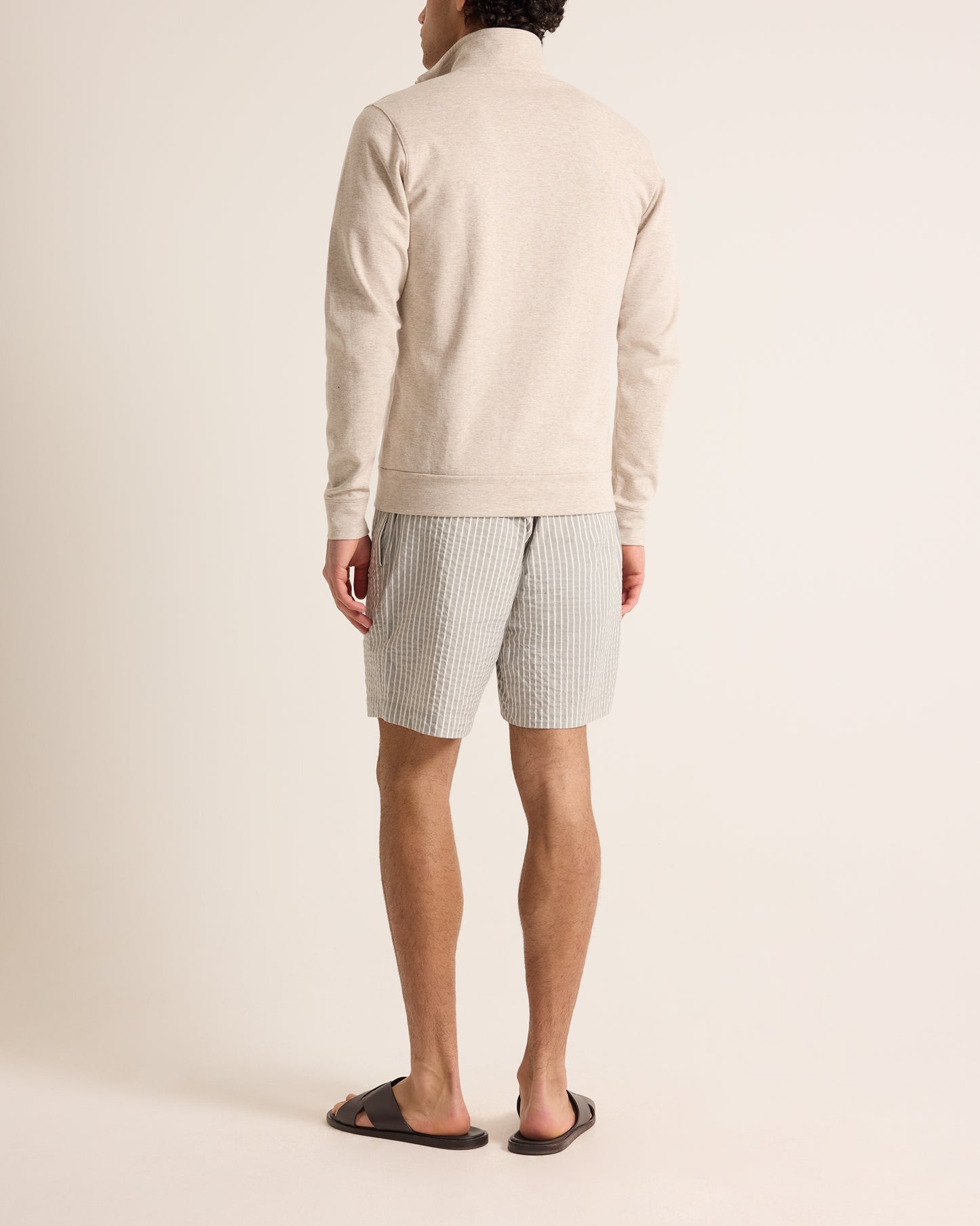 Person wearing a cream sweater and striped shorts on a plain background