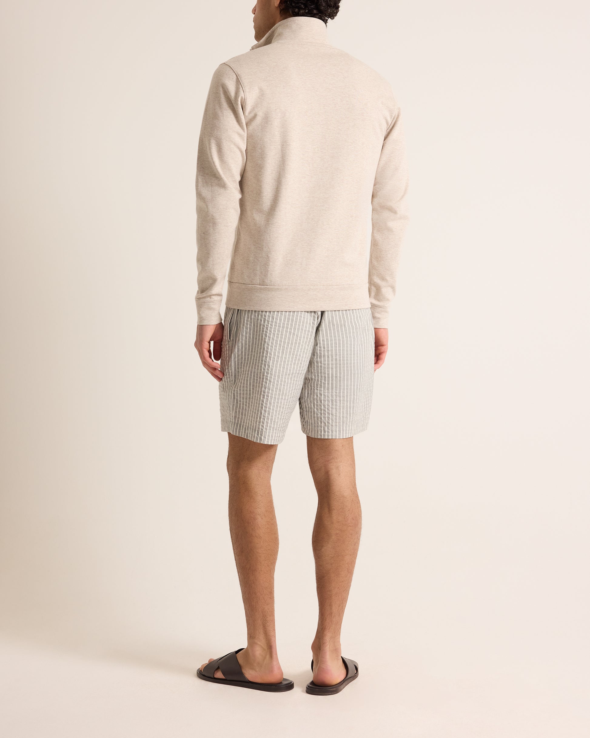 Person wearing a cream sweater and striped shorts on a plain background