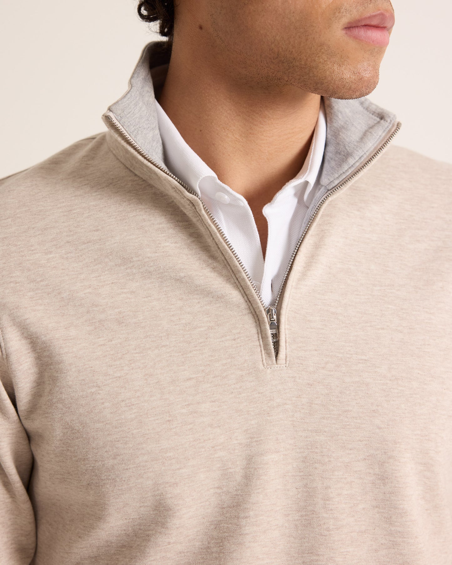 Close-up of a person wearing a beige half-zip sweater over a white shirt.