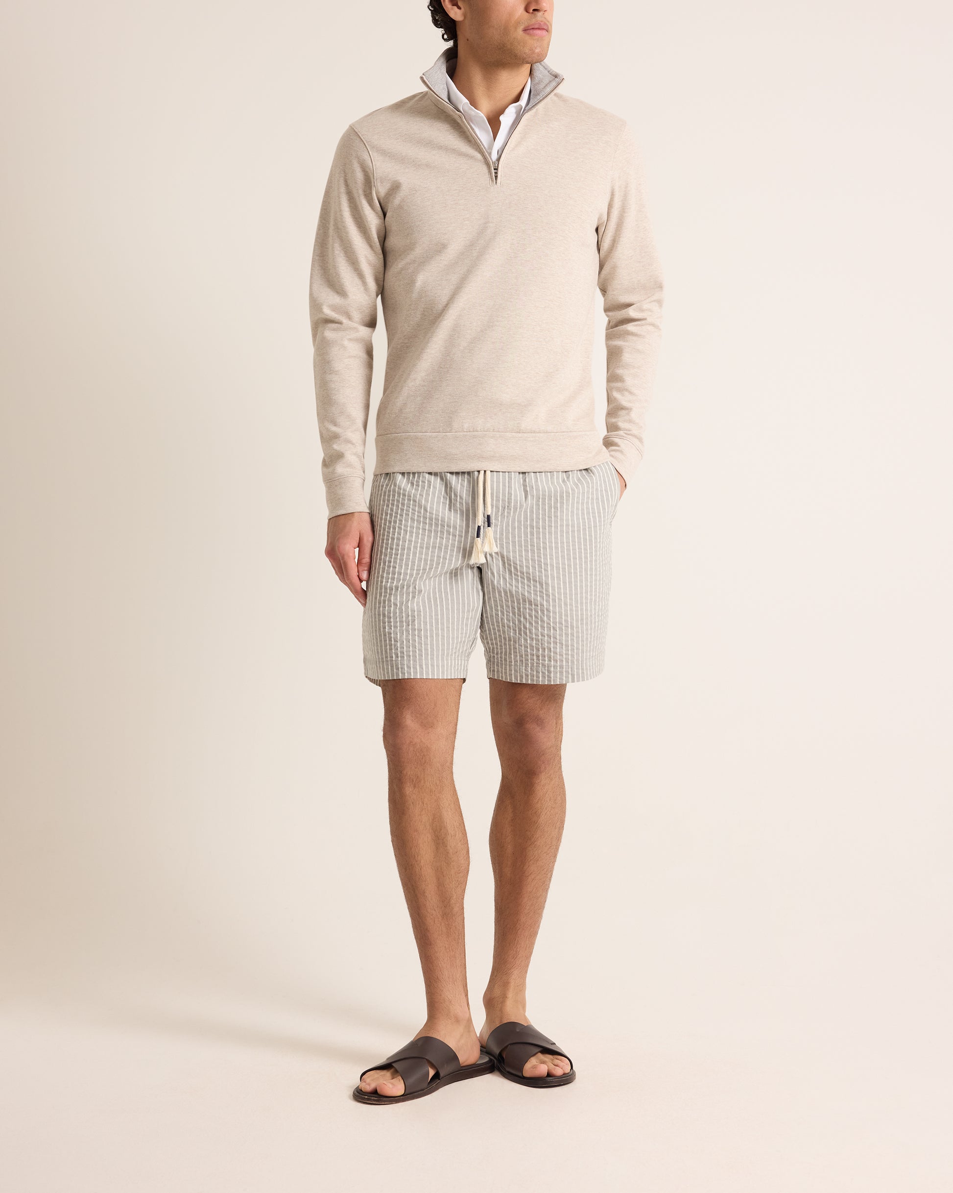 Man wearing a beige sweater and striped shorts on a plain background