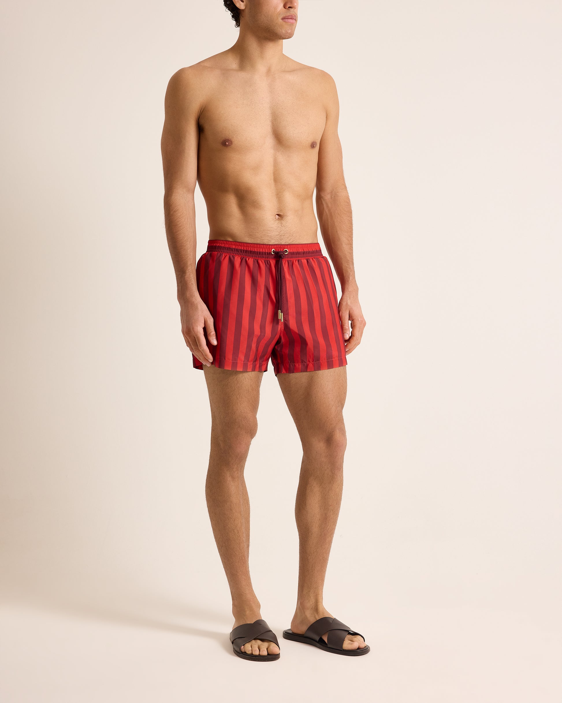 Man wearing red striped swim shorts on a beige background