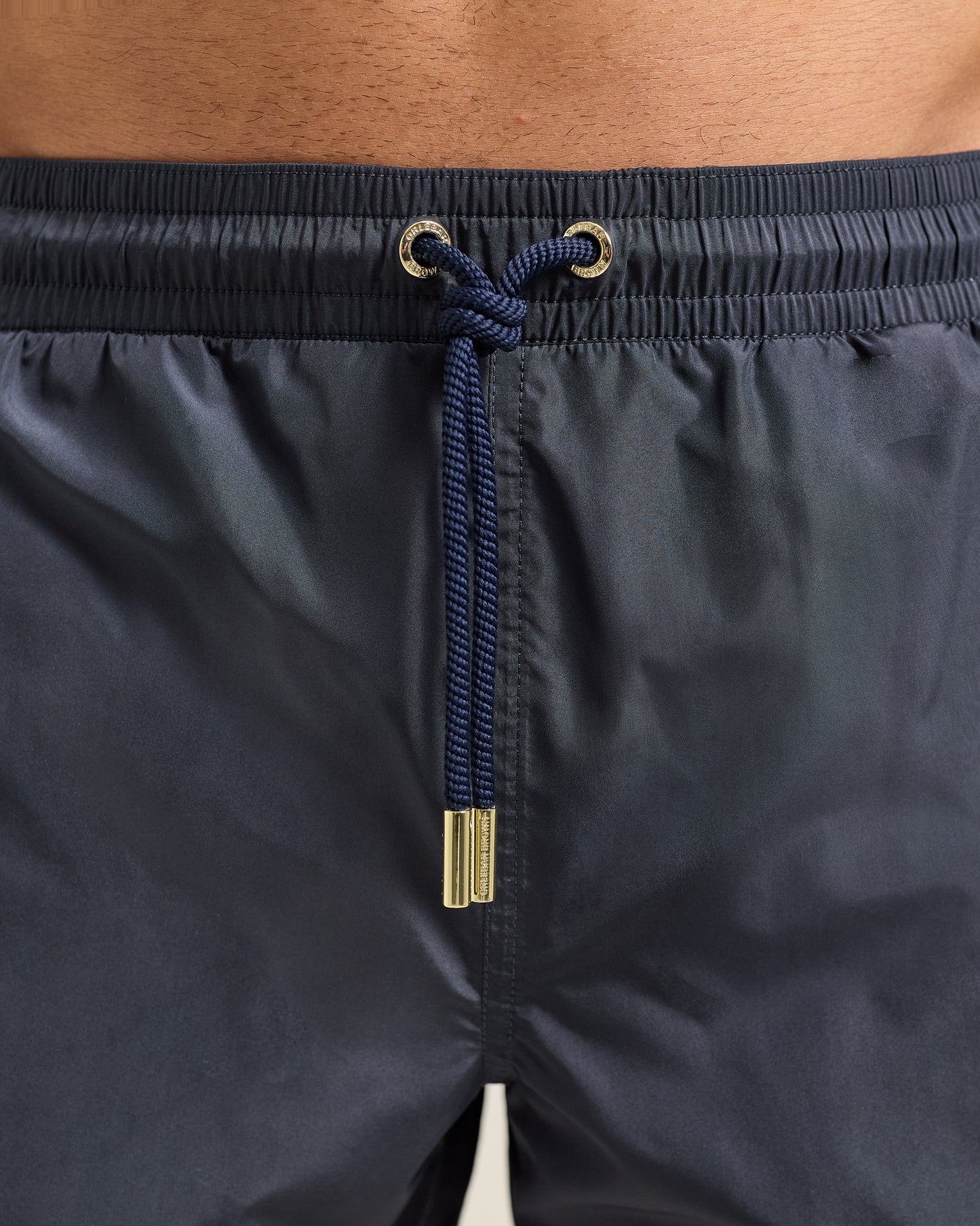 Navy swim shorts with drawstring and metal buckle on a neutral background
