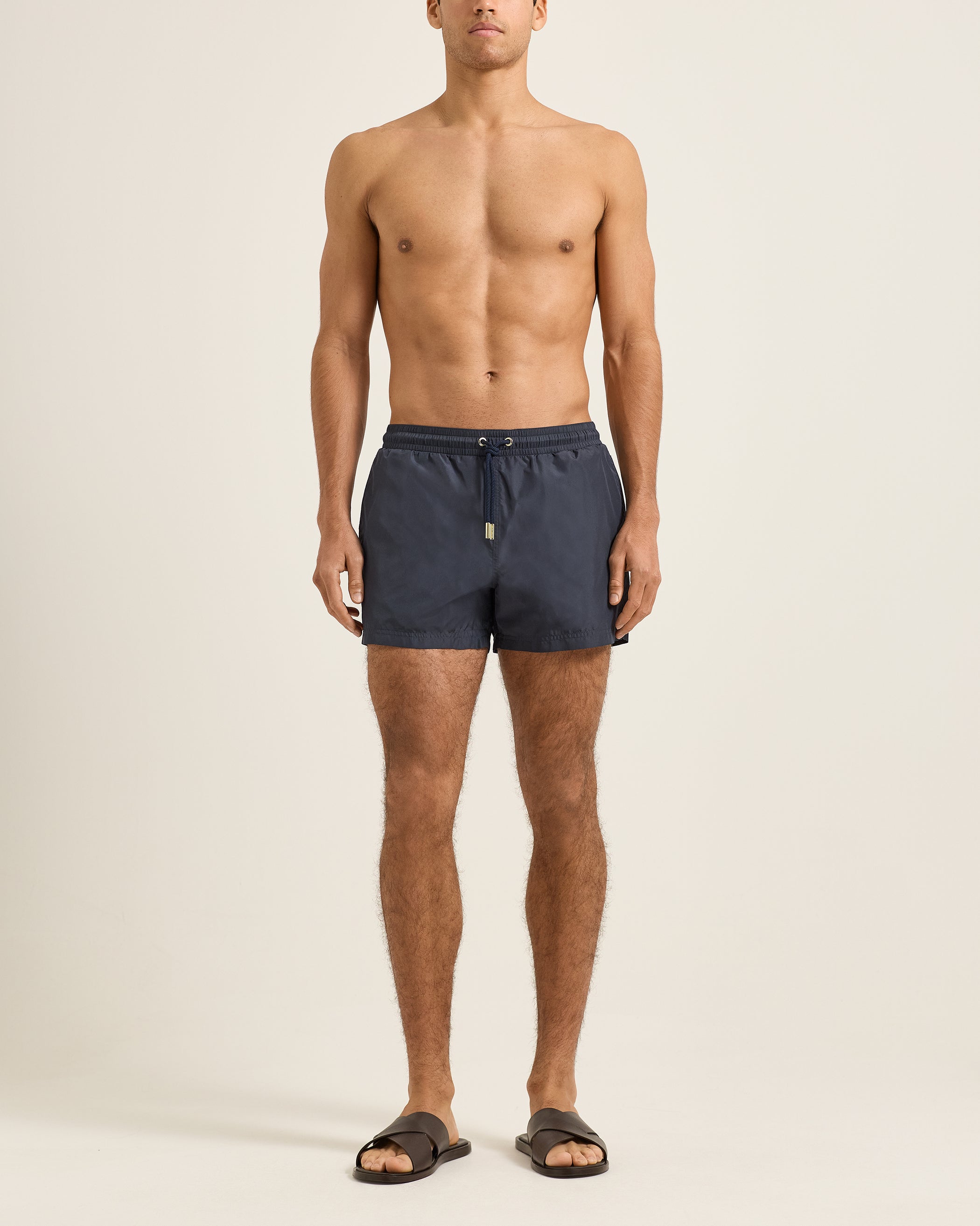 Man wearing navy blue swim shorts on a beige background