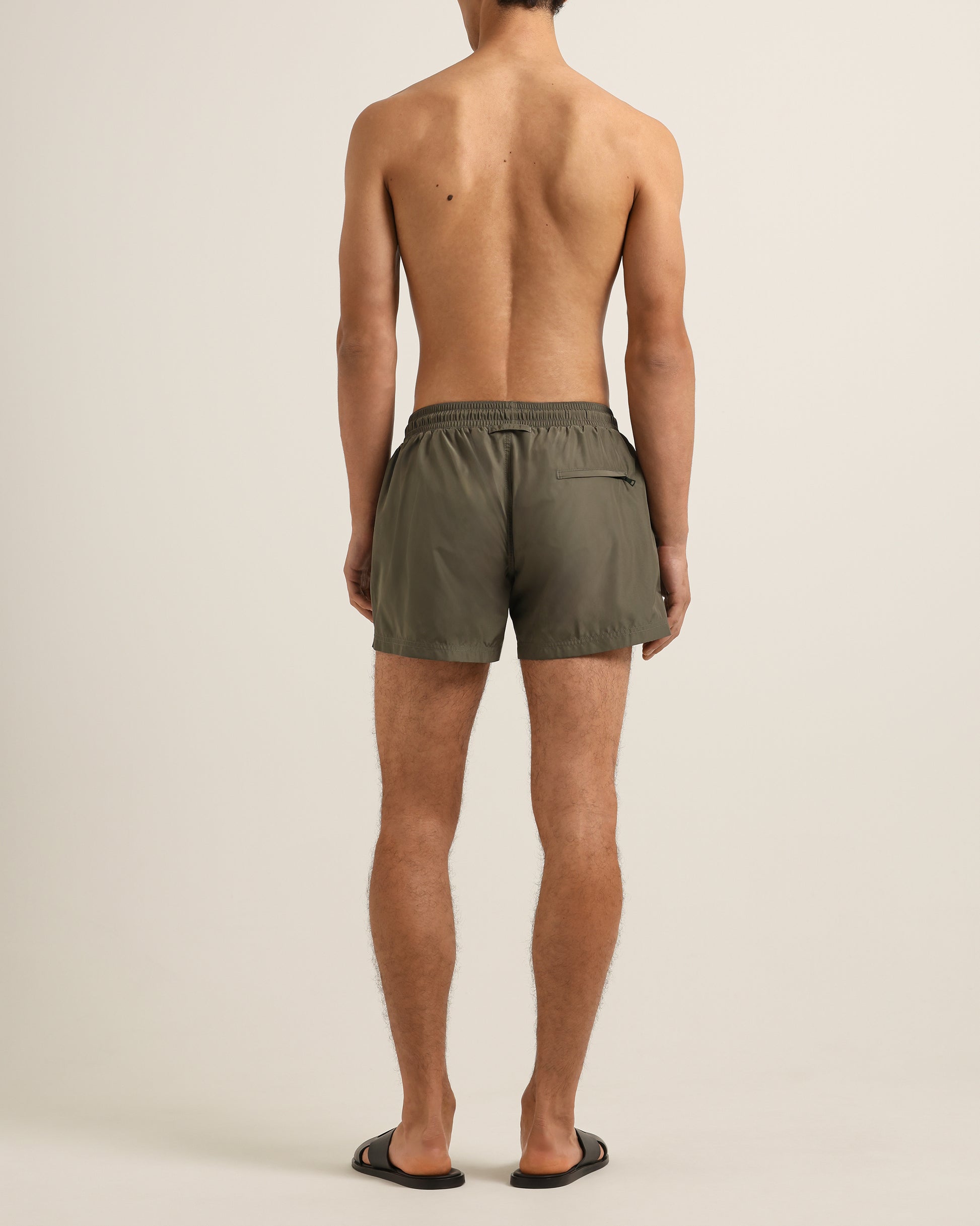 Person wearing olive green shorts on a beige background