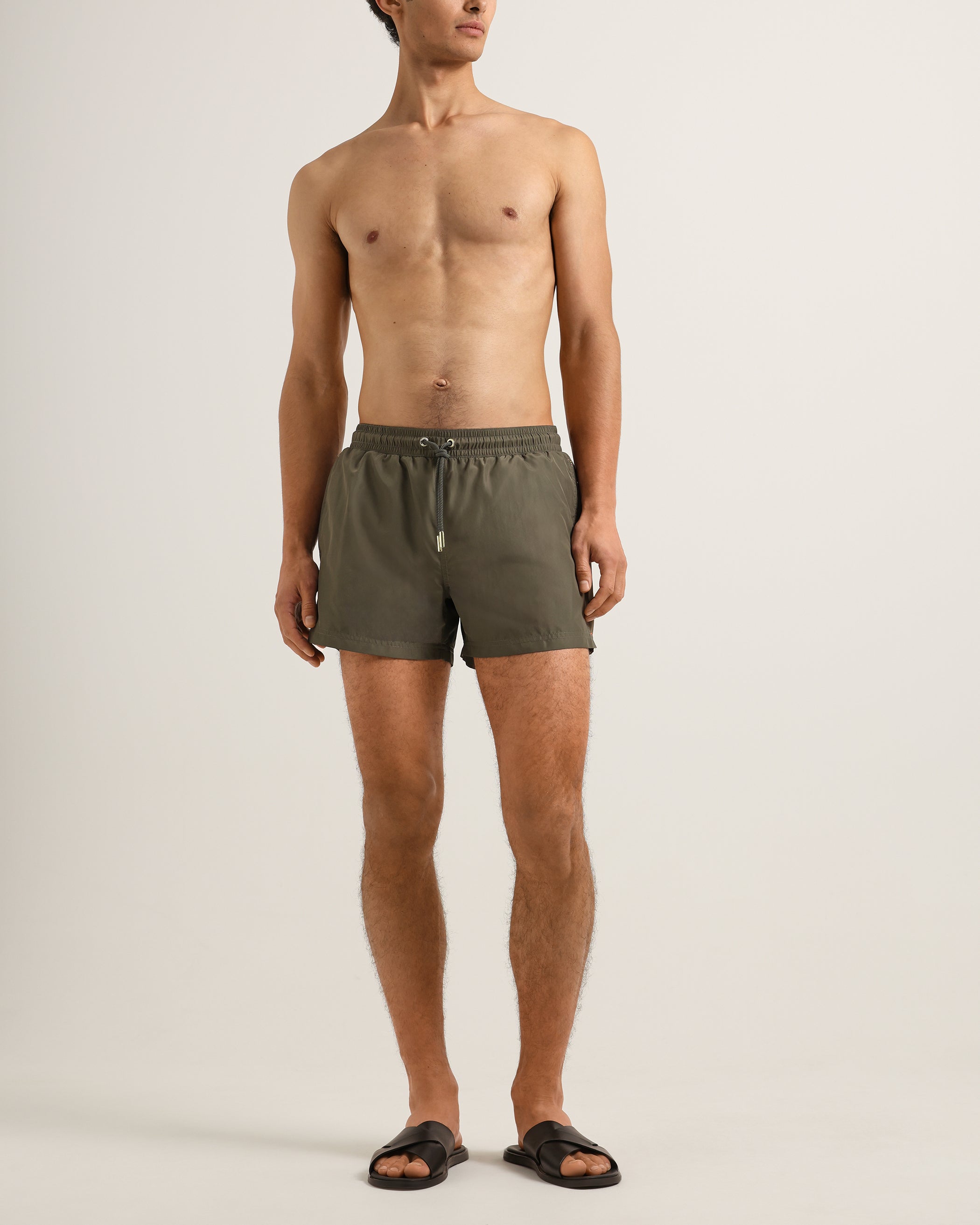 Man wearing olive green swim shorts on a plain background