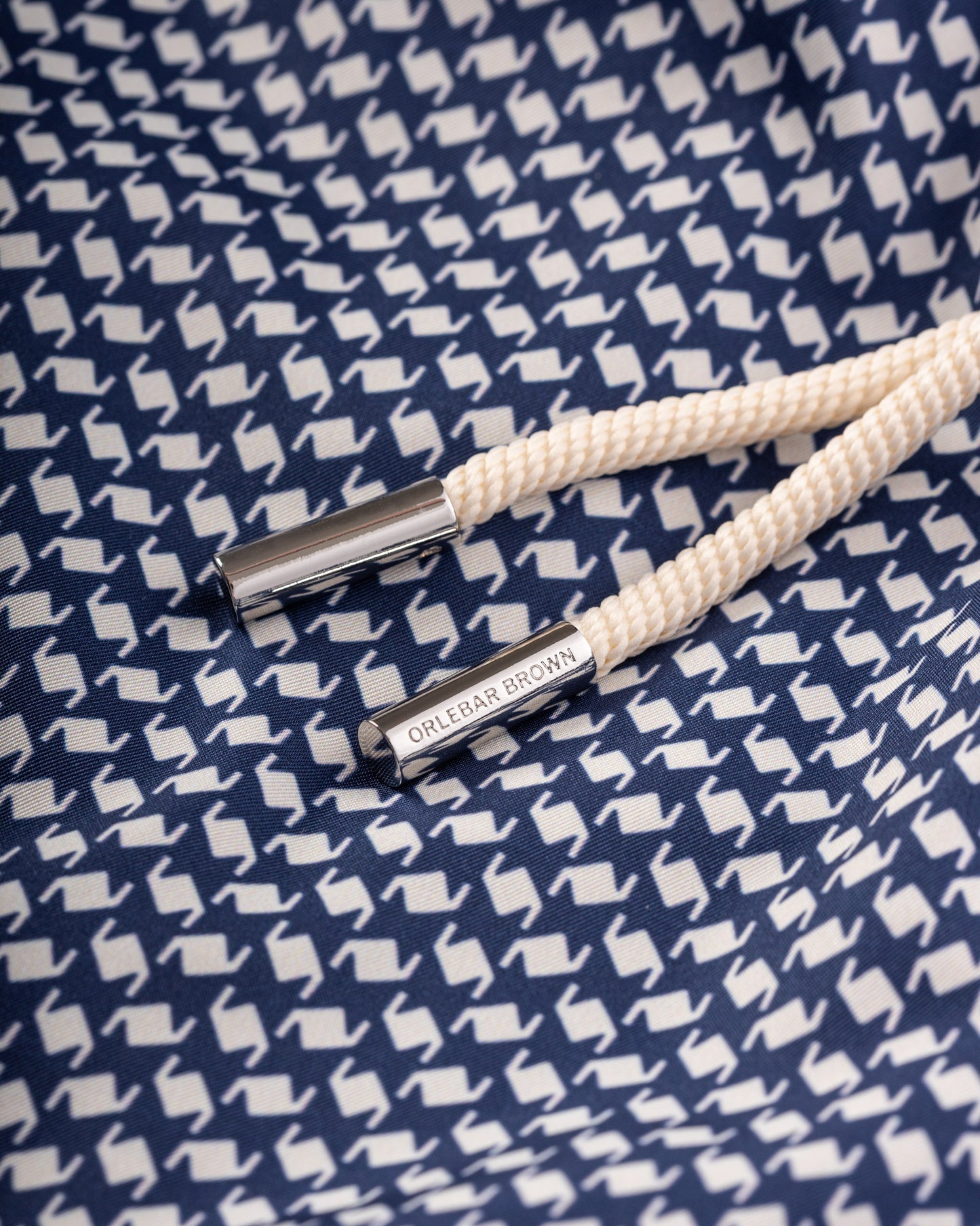 White rope tie with silver clasp on a blue fabric background with white patterns