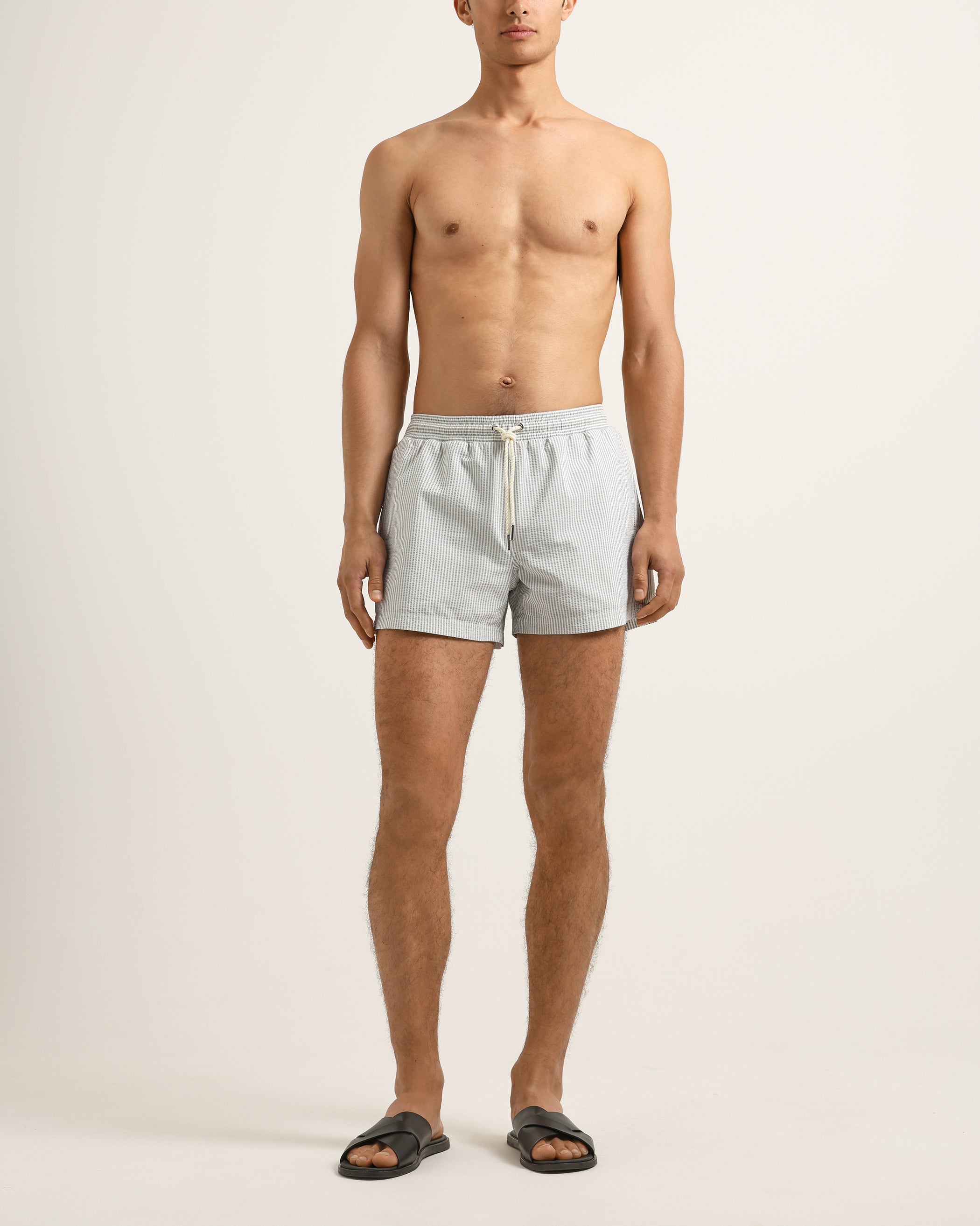 Man wearing light gray swim shorts on a plain background