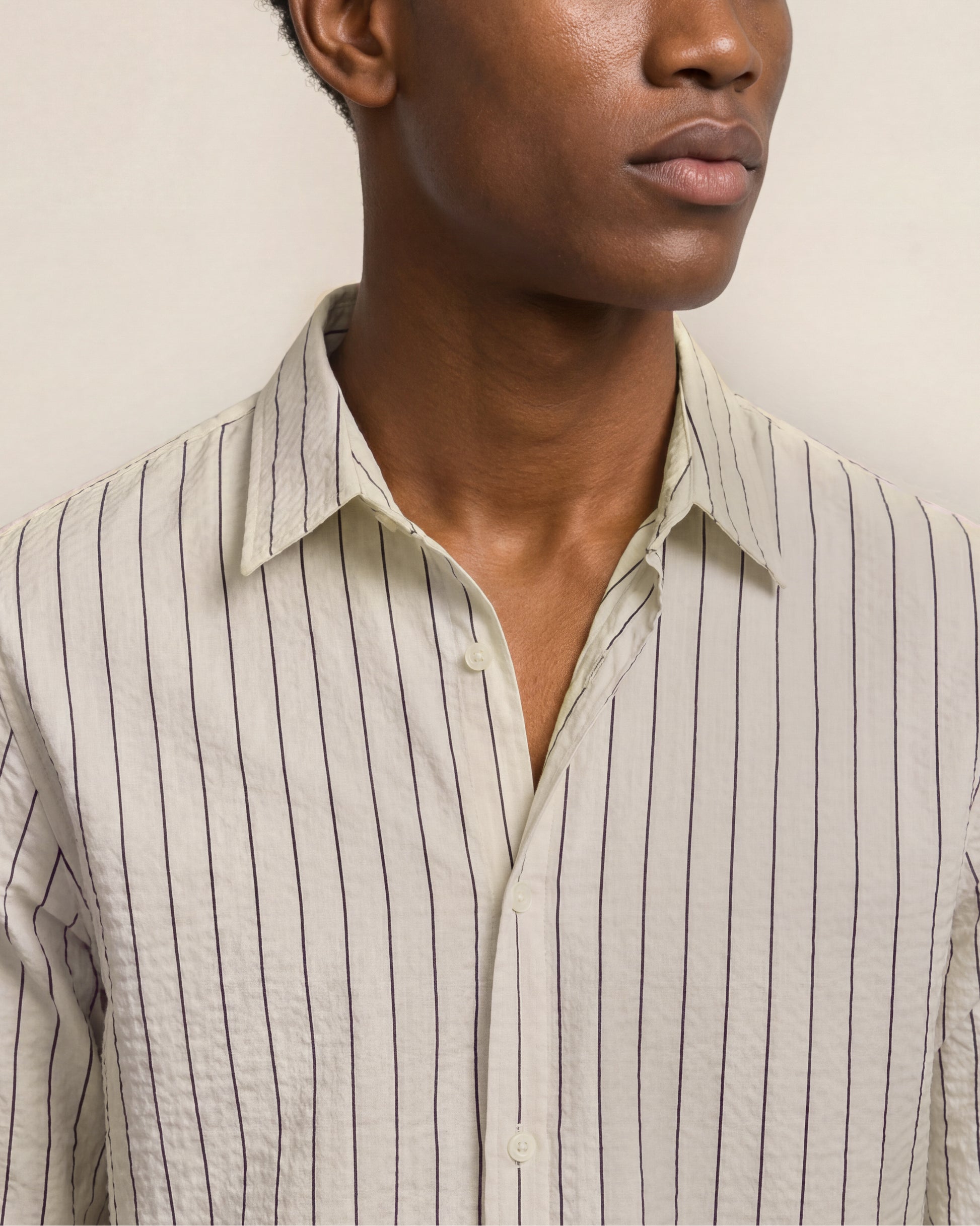 Close-up of a person wearing a beige striped shirt against a neutral background