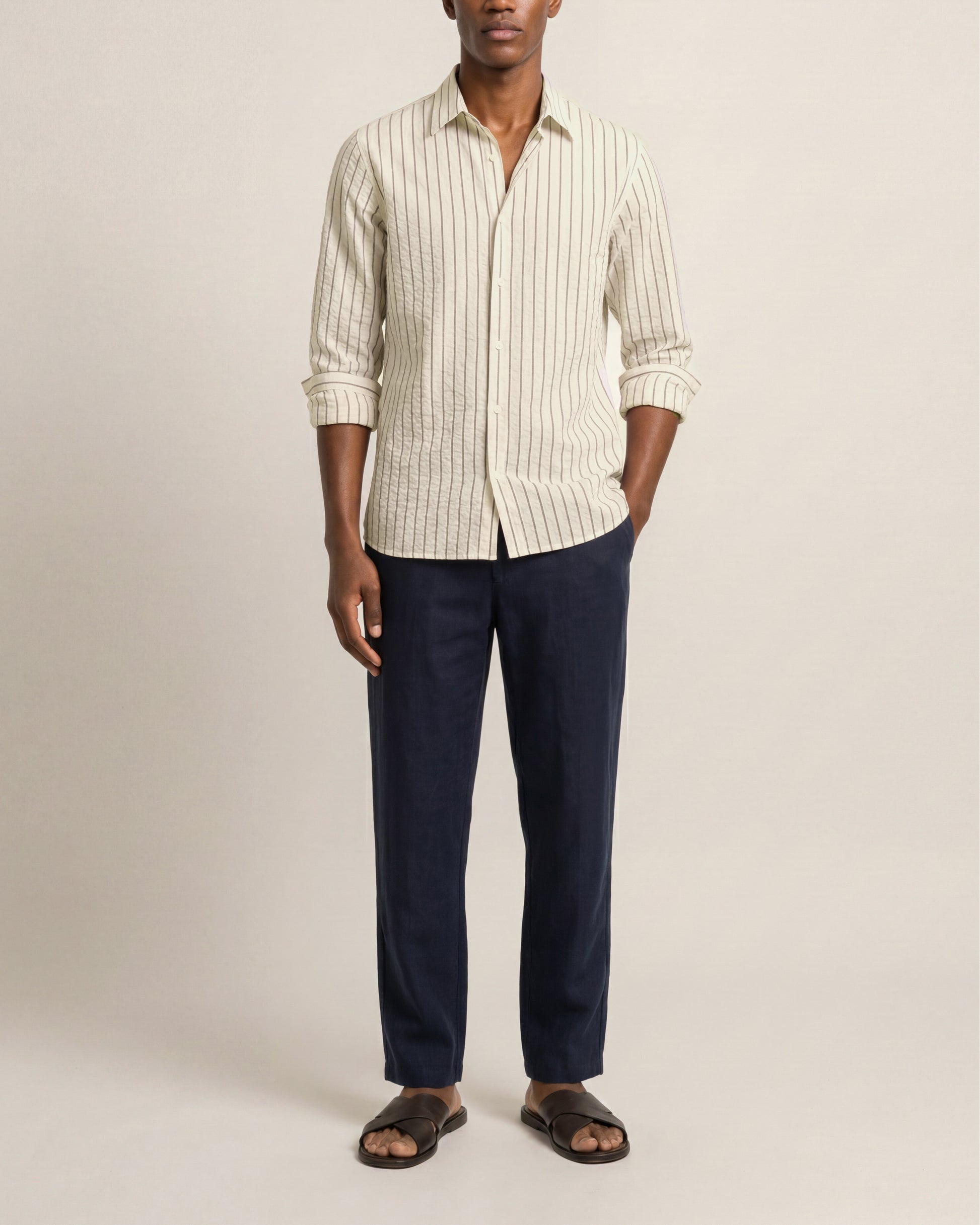 Man wearing a white striped shirt and dark pants on a beige background