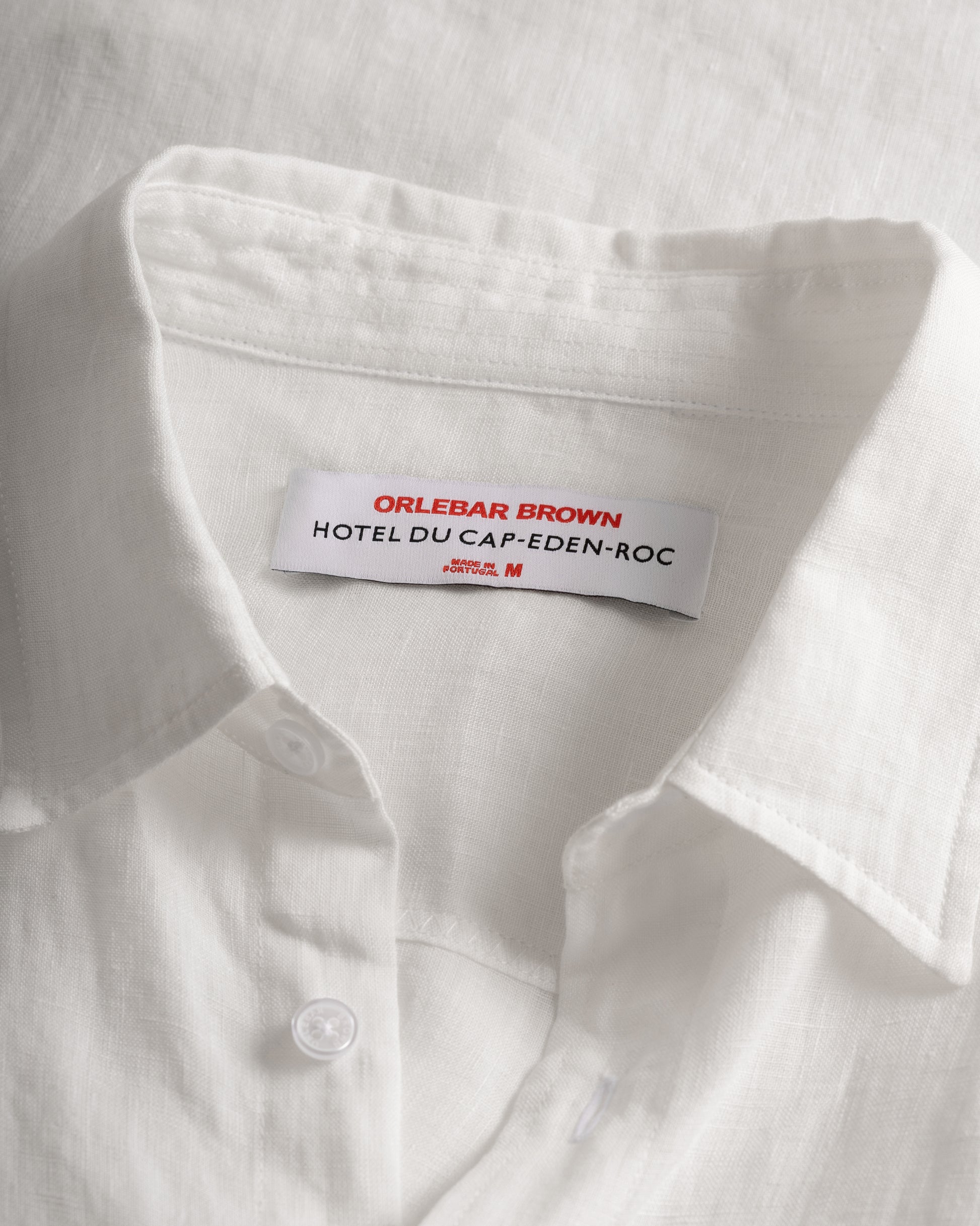 Close-up of a white linen button-down shirt collar with a visible brand label reading ORLEBAR BROWN HOTEL DU CAP-EDEN-ROC.