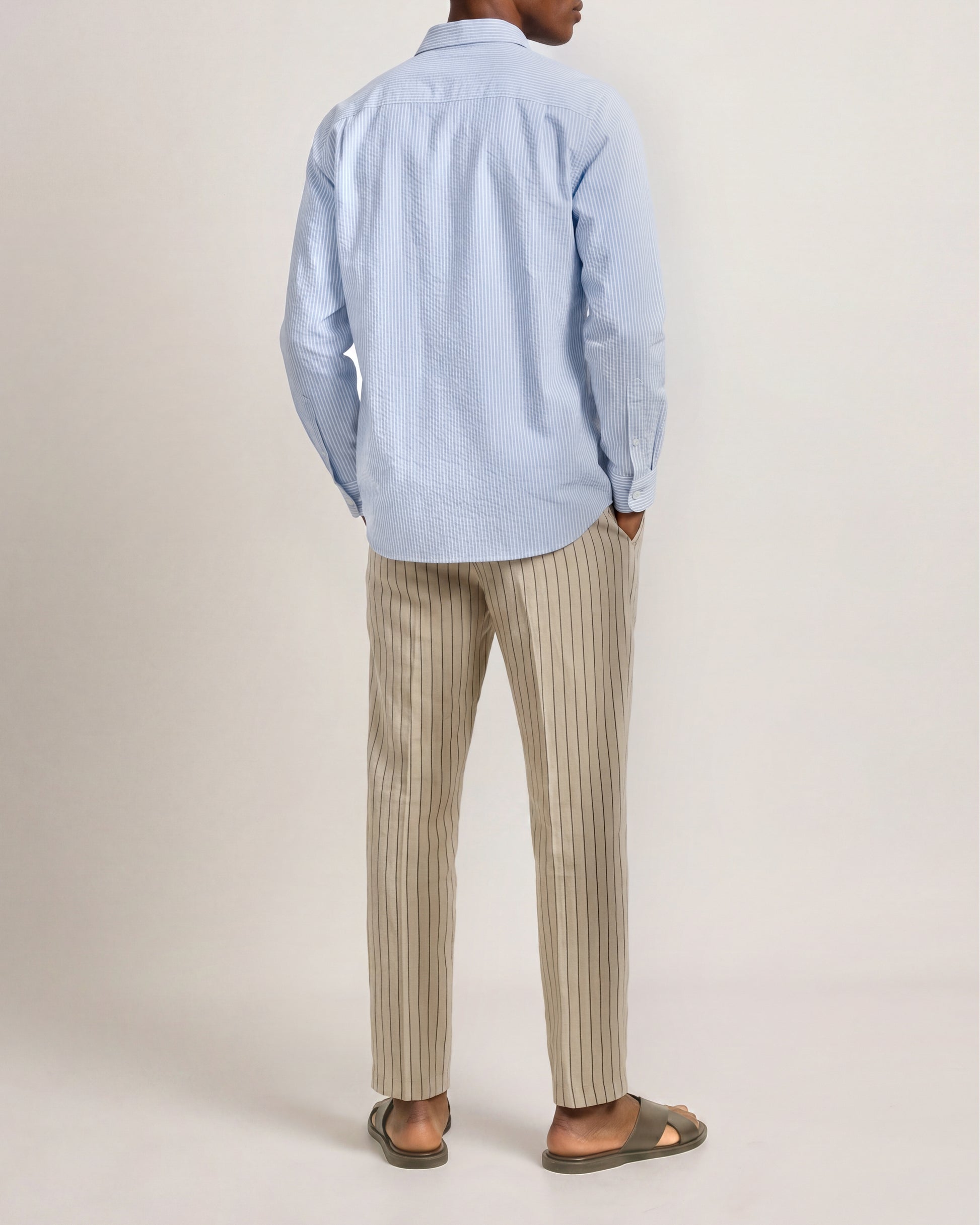 Person wearing a light blue shirt and beige striped pants on a plain background