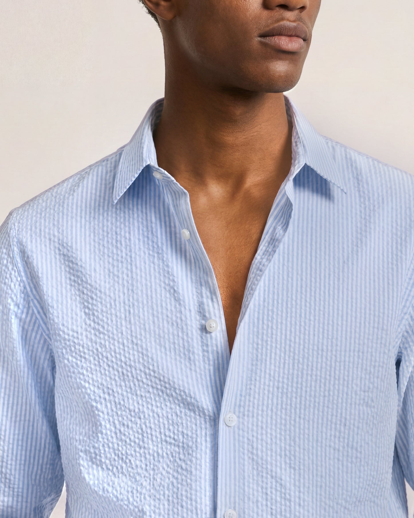 Man wearing a light blue striped shirt against a neutral background
