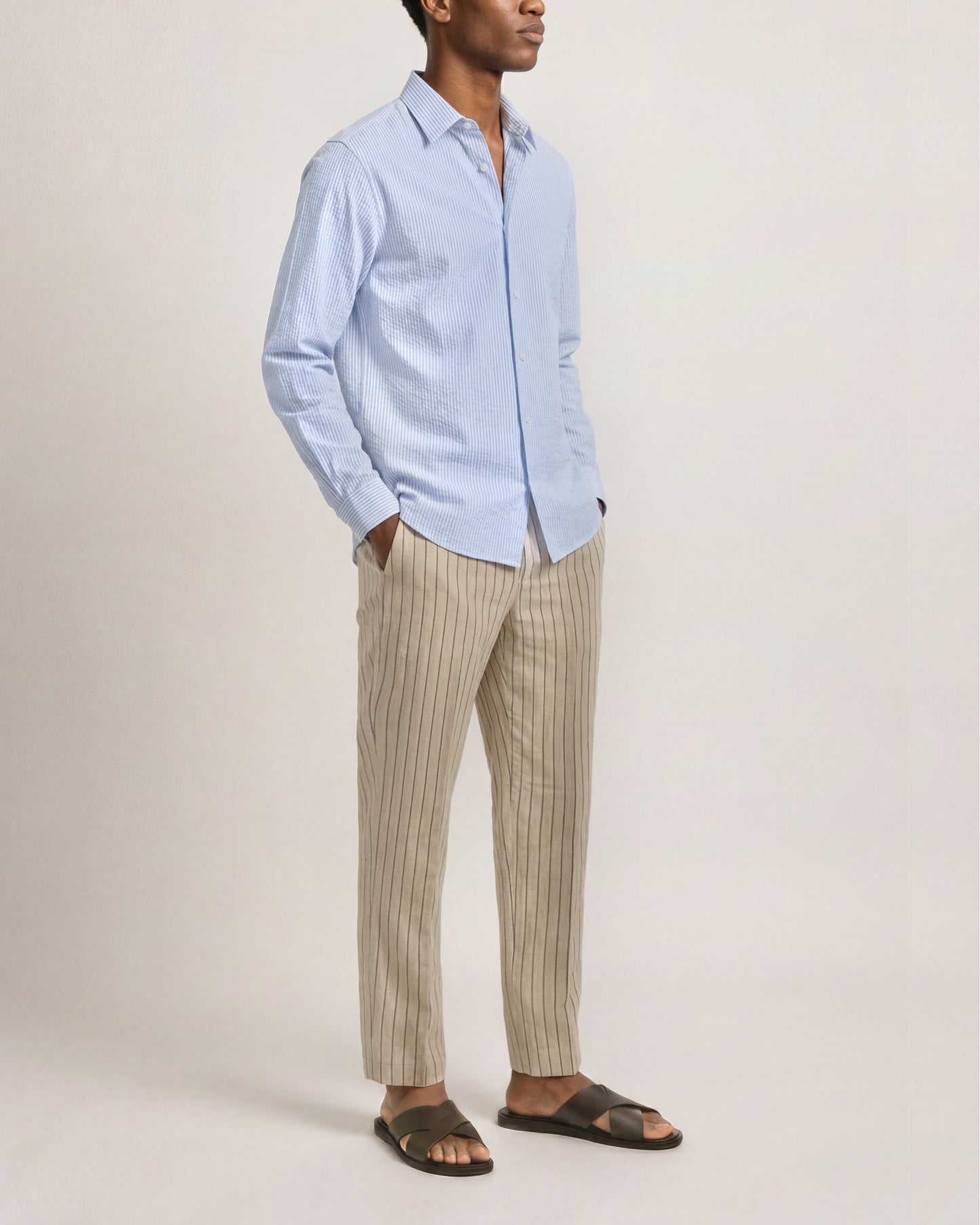 Person wearing a light blue shirt and beige striped pants on a plain background