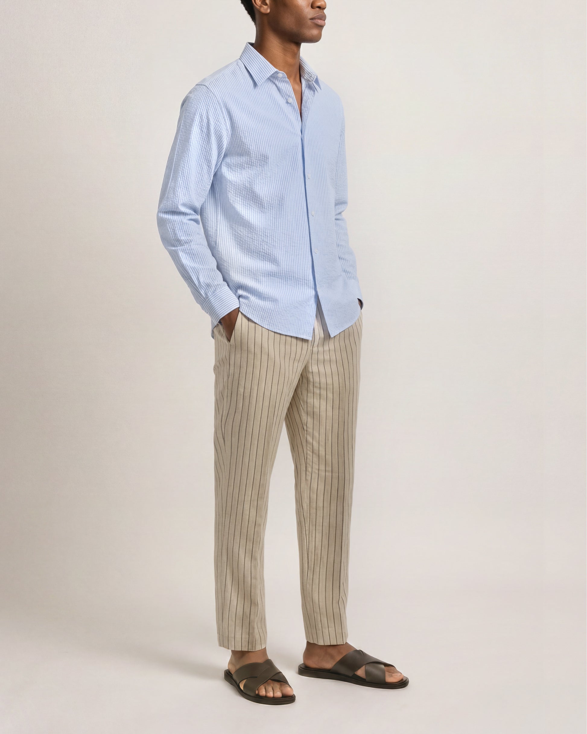 Person wearing a light blue shirt and beige striped pants on a plain background