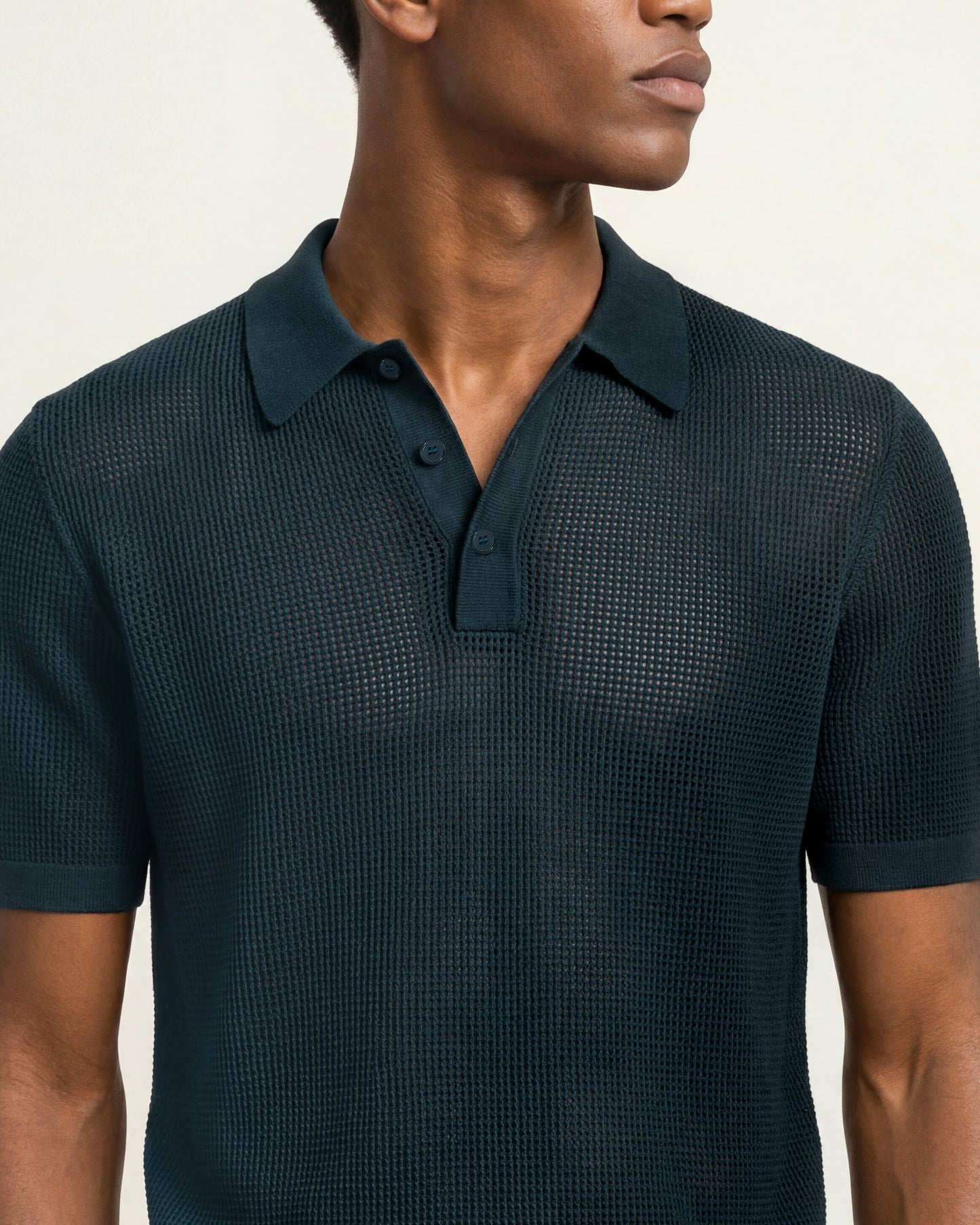 A close-up of a man wearing a dark teal textured short-sleeve polo shirt against a plain light background.