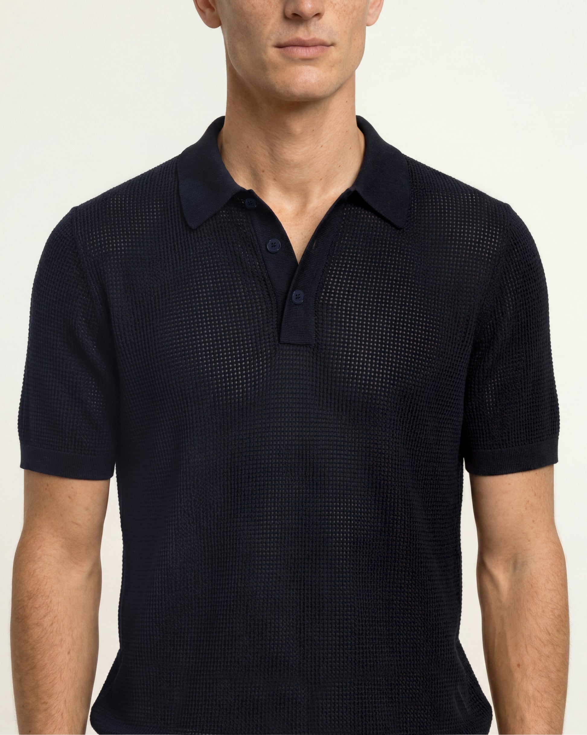 A man wearing a dark navy blue short-sleeve polo shirt with a subtle textured grid pattern, shown from the chest up against a plain light background.