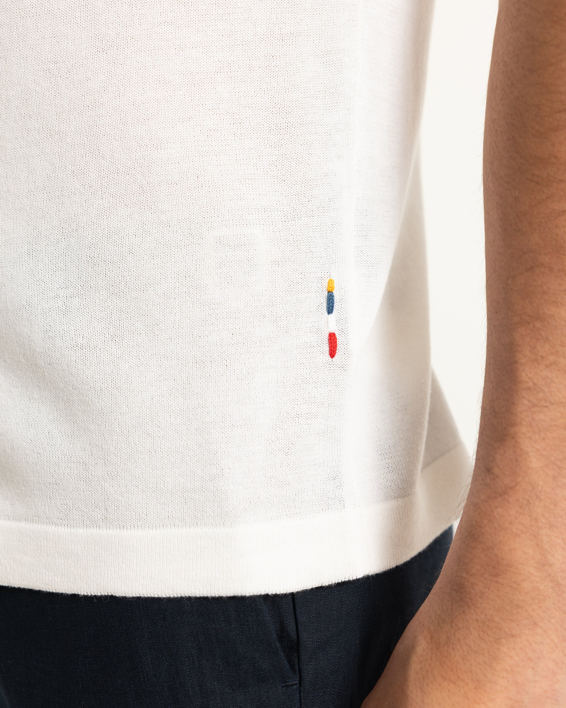 Close-up of a white t-shirt with colorful logo on a person wearing navy pants.