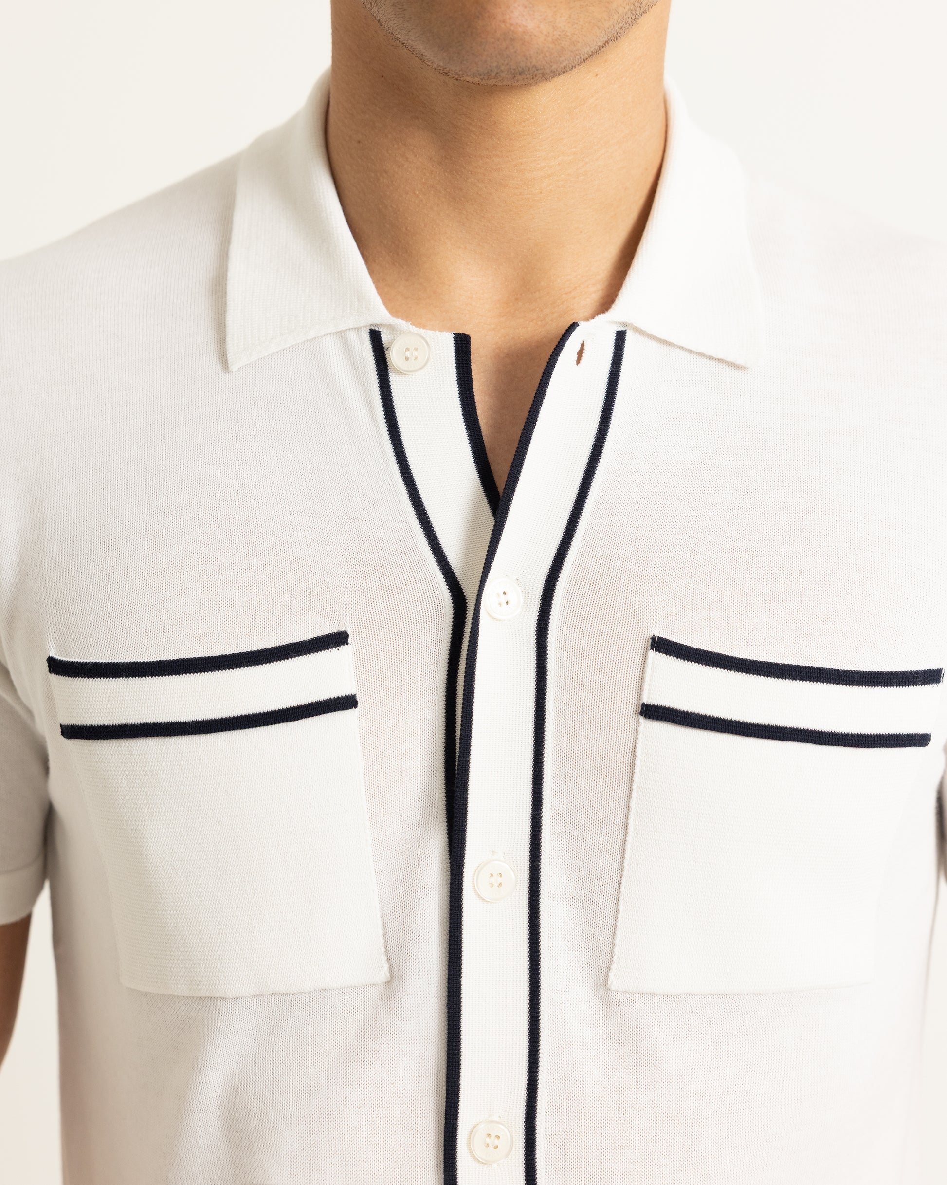 Close-up of a white shirt with black trim on a plain background