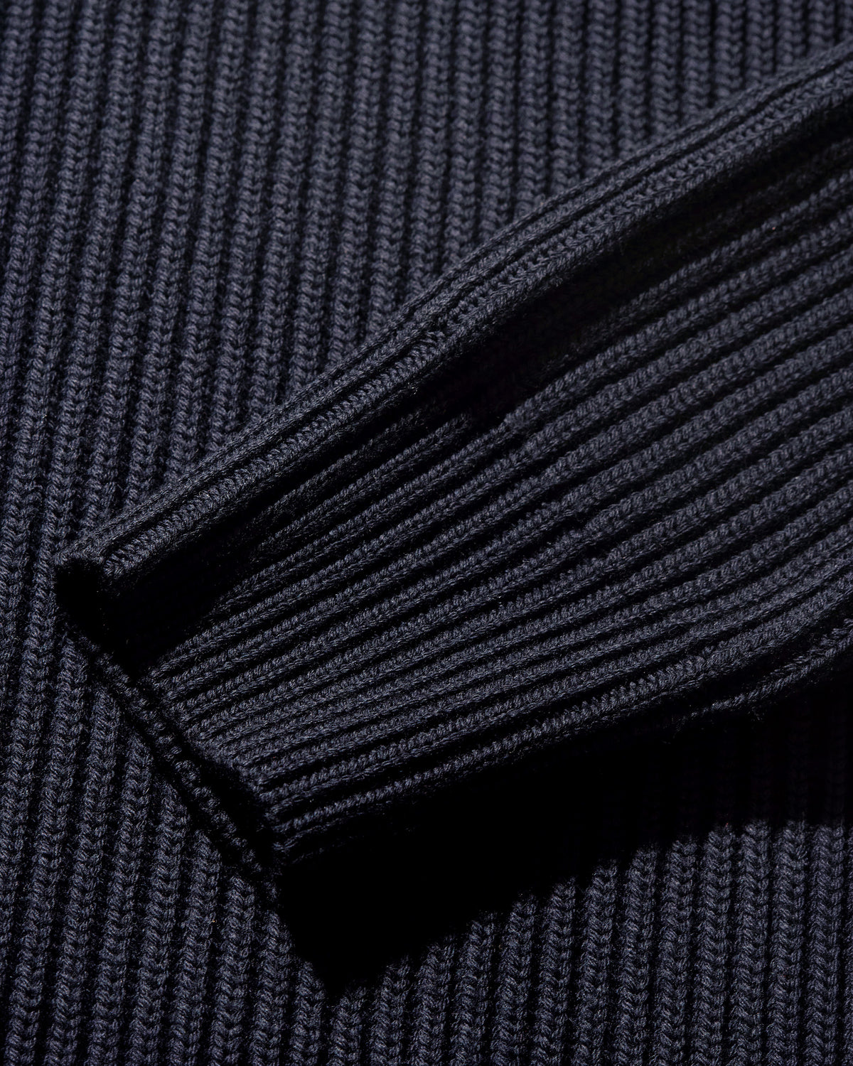 Close-up of a dark navy ribbed knit fabric, showing the detailed texture of the ribbed cuff or sleeve.