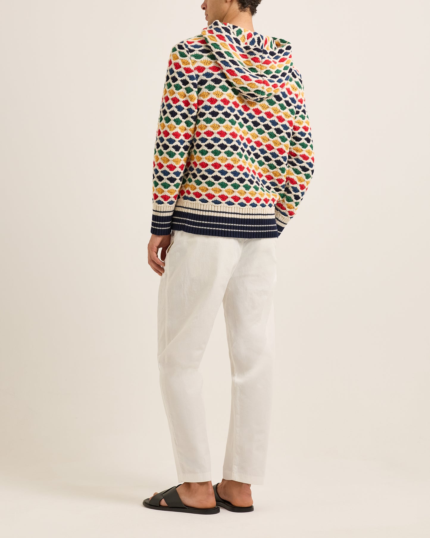 Person wearing a colorful patterned sweater and white pants on a plain background