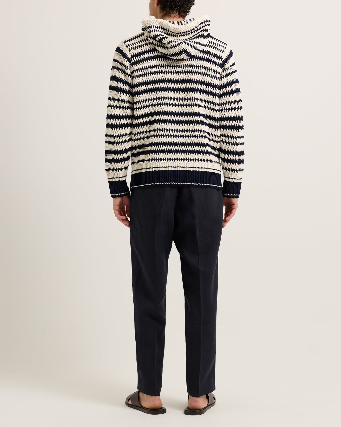 Man wearing knitted striped hoodie with navy trousers on a white background