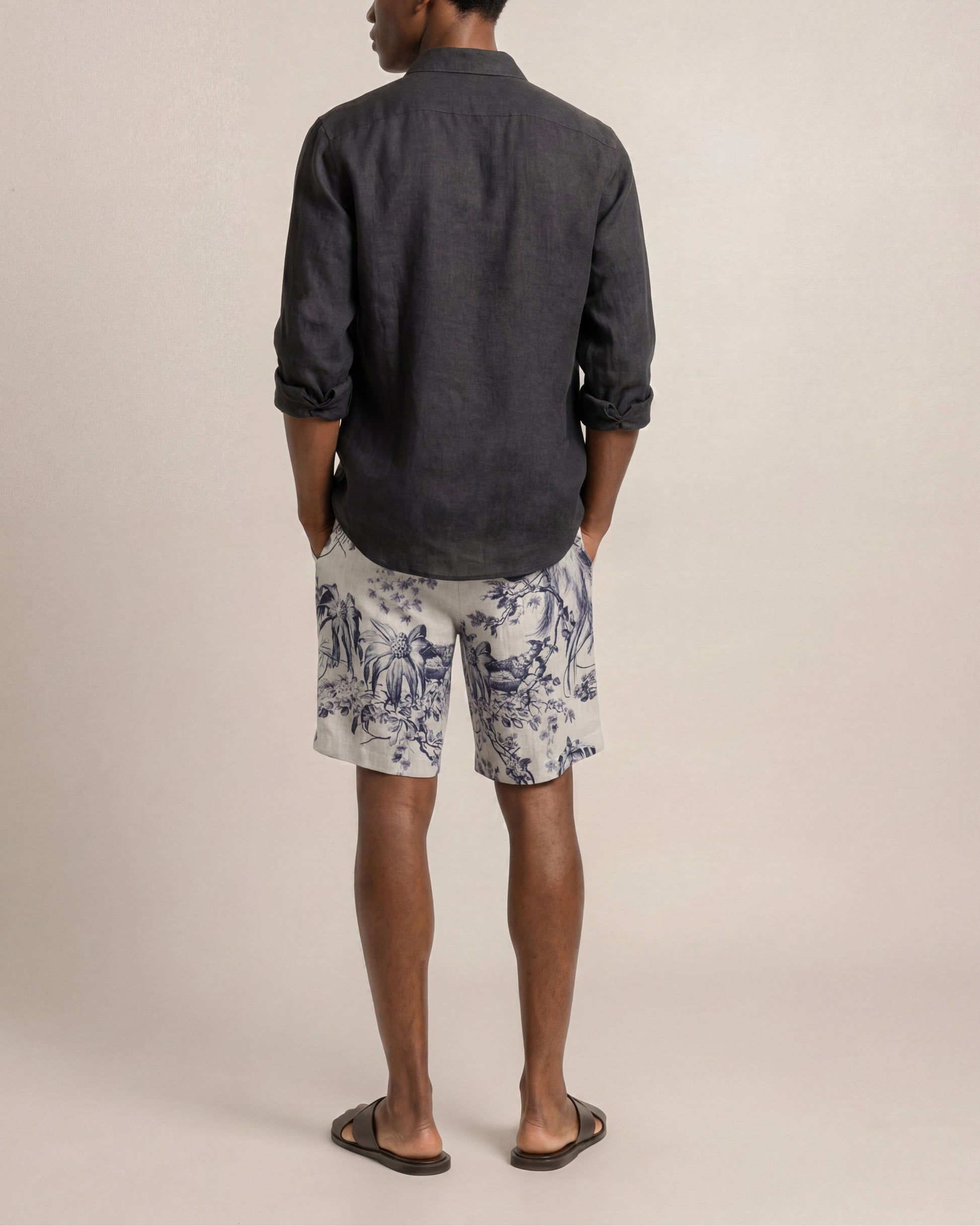 Person wearing a dark shirt and patterned shorts on a plain background