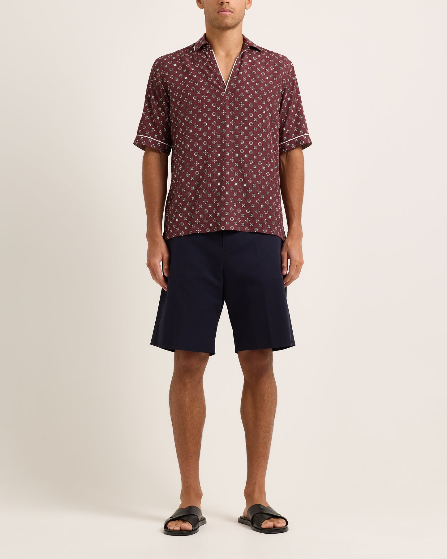 Model wearing navy shorts with maroon patterned shirt on a plain background