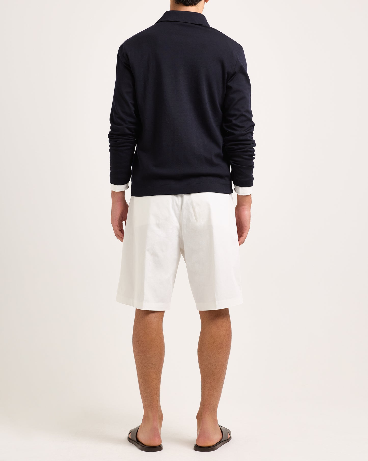 Model wearing white shorts with navy long sleeve polo shirt on a plain background