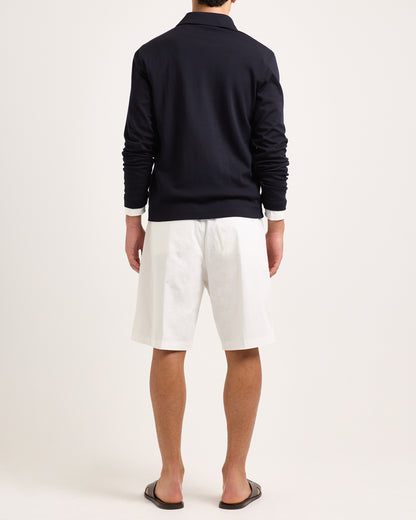 Model wearing white shorts with navy long sleeve polo shirt on a plain background