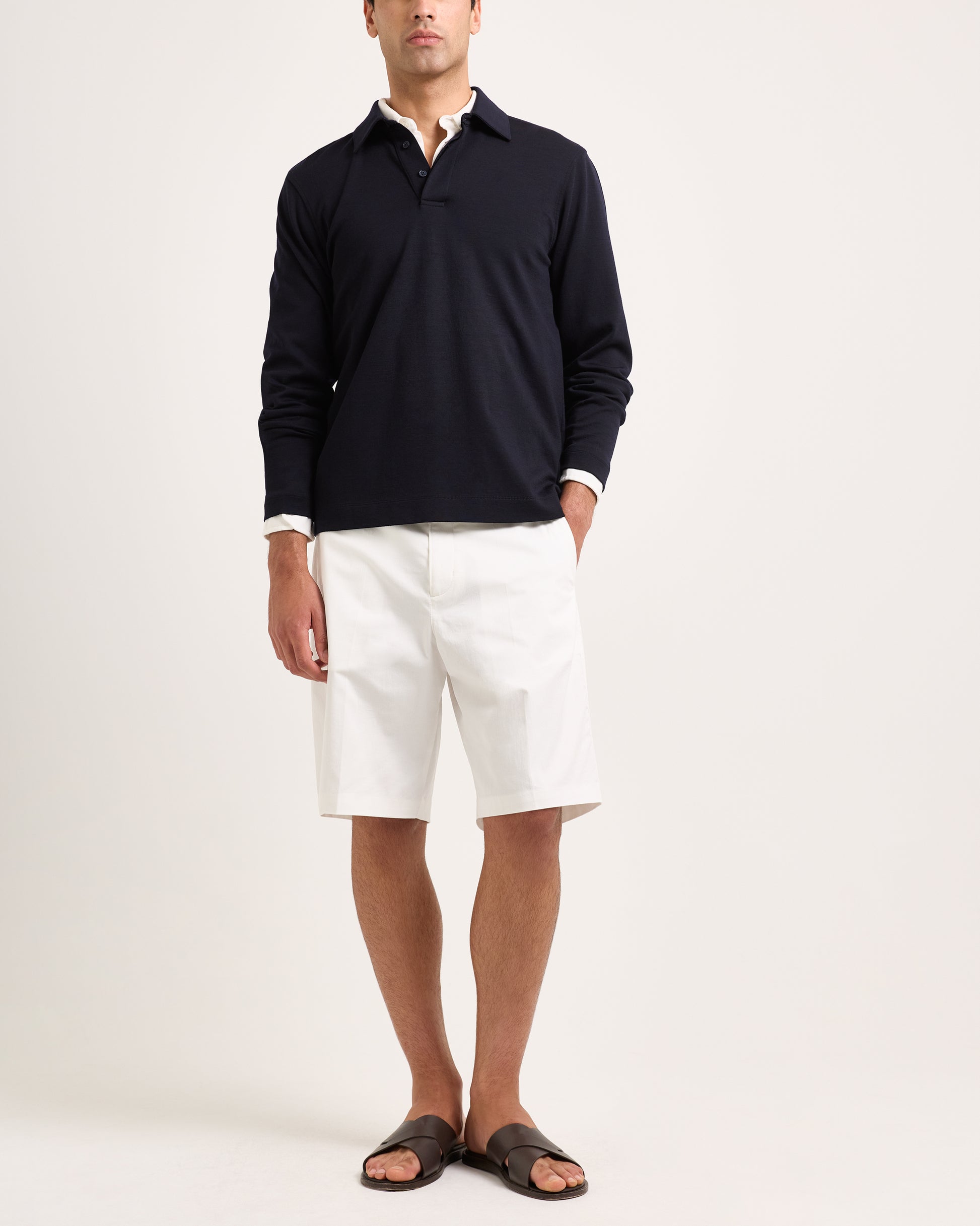 Model wearing white shorts with navy long sleeve polo shirt on a plain background