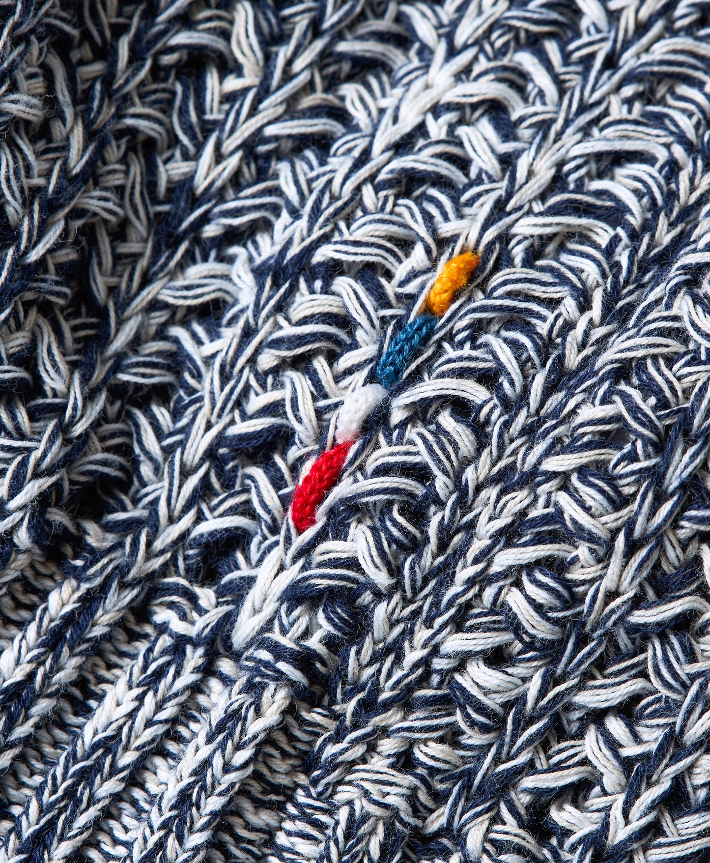 Close-up of a textured knit fabric in navy blue and white, featuring a small colorful accent with red, blue, yellow, and white threads.