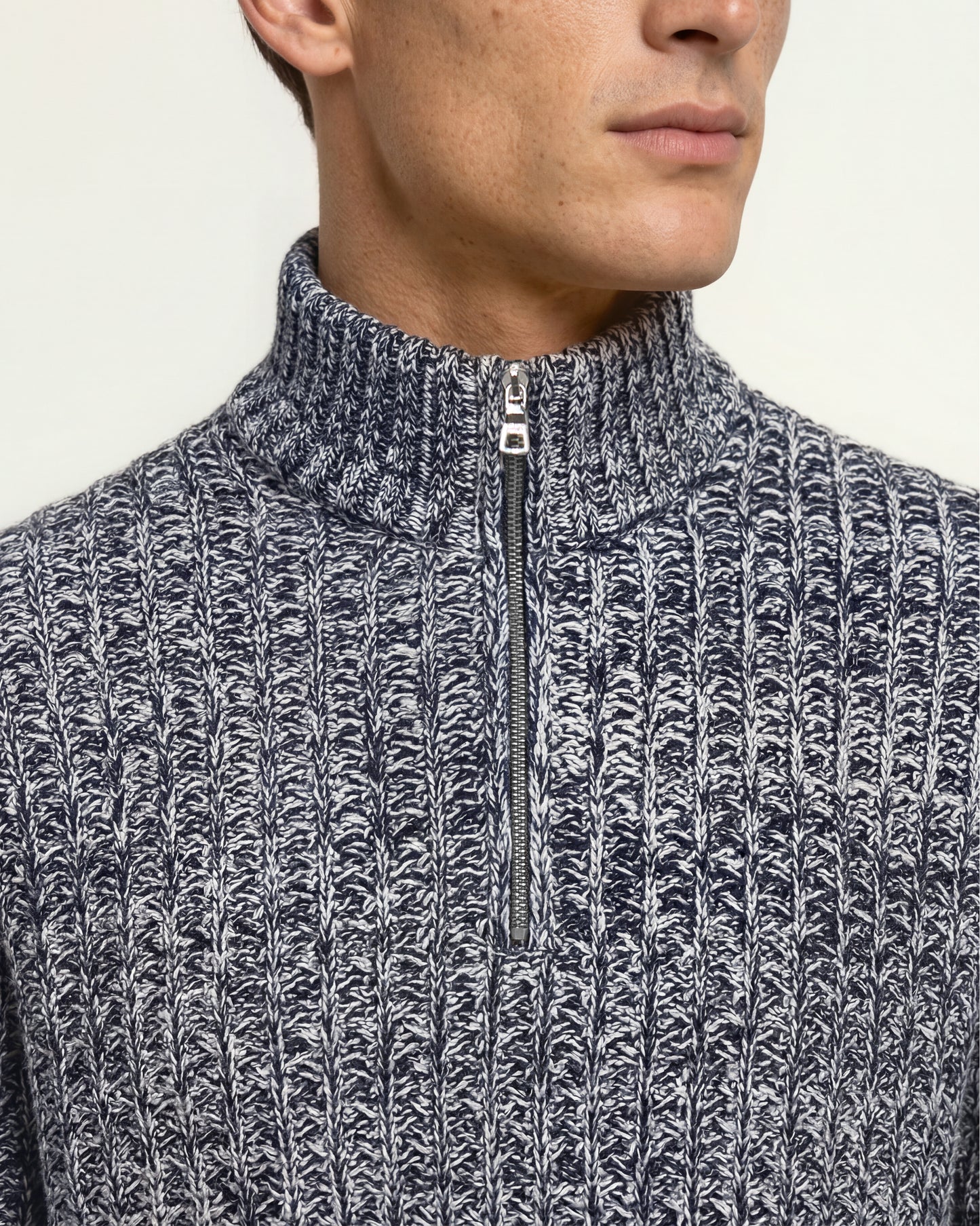 Close-up of a man wearing a navy and white marled knit quarter-zip sweater with a ribbed mock neck collar.