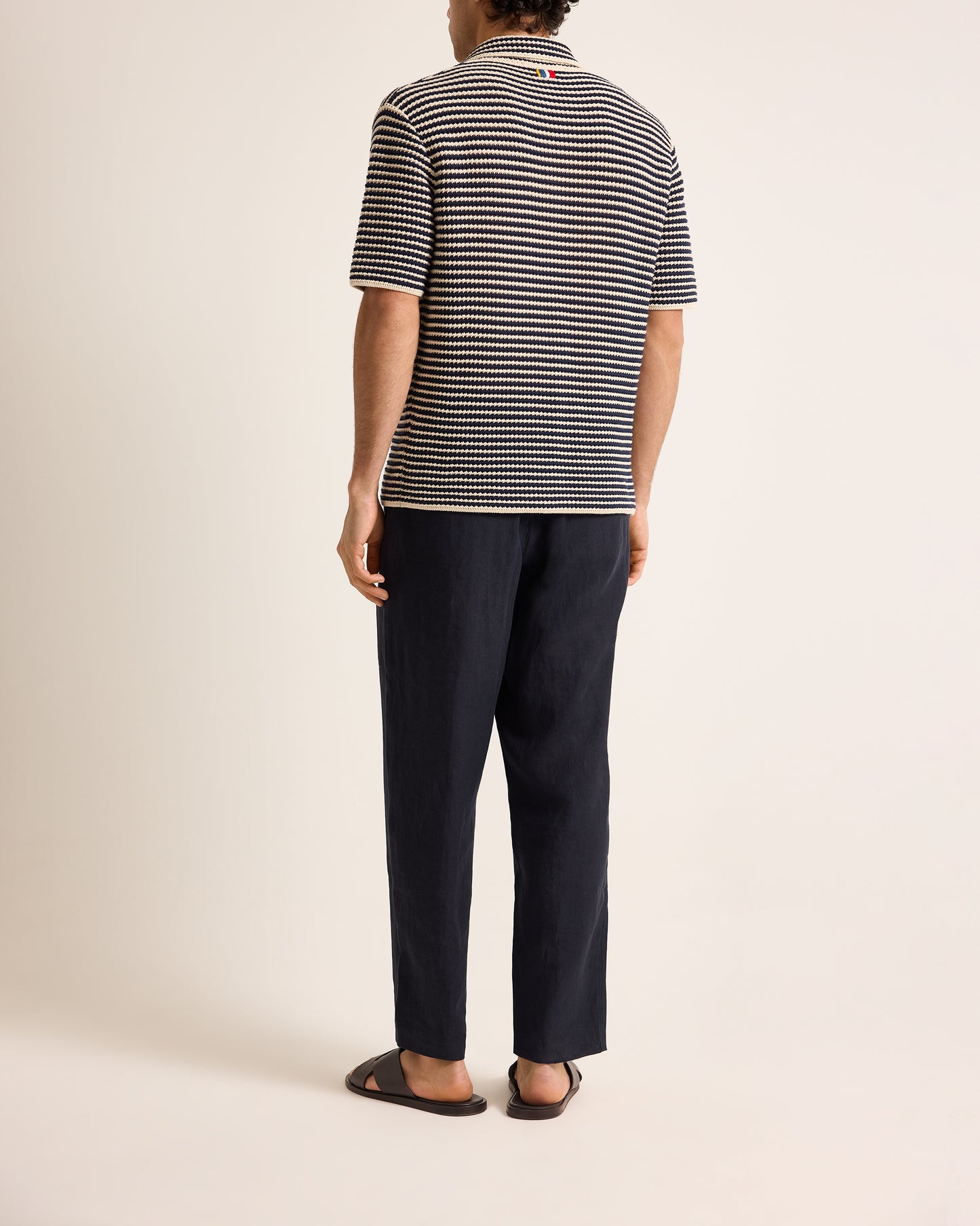 Person wearing a striped polo shirt and dark pants on a plain background