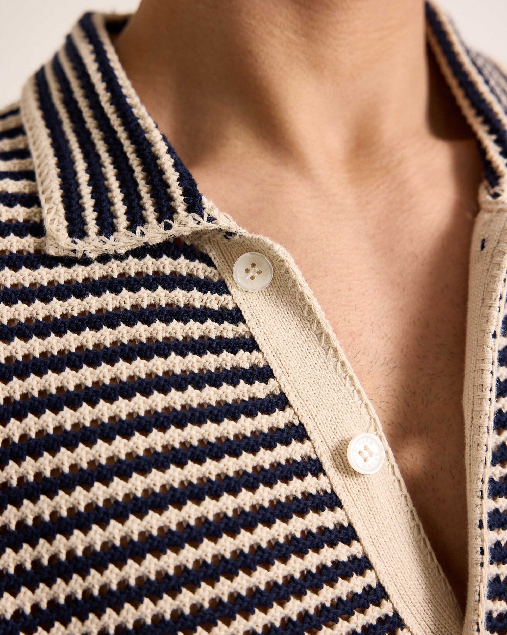 Close-up of a person wearing a navy and beige striped shirt with a buttoned collar.