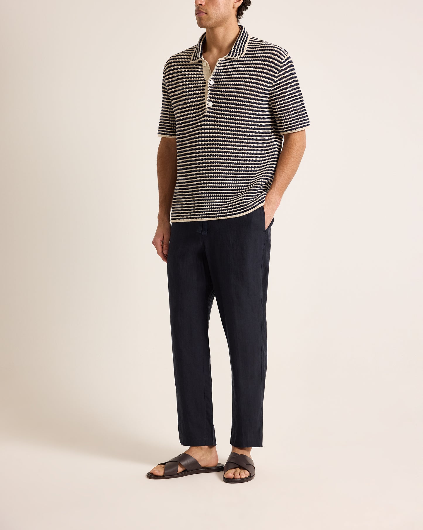 Man wearing a striped polo shirt and dark pants on a plain background