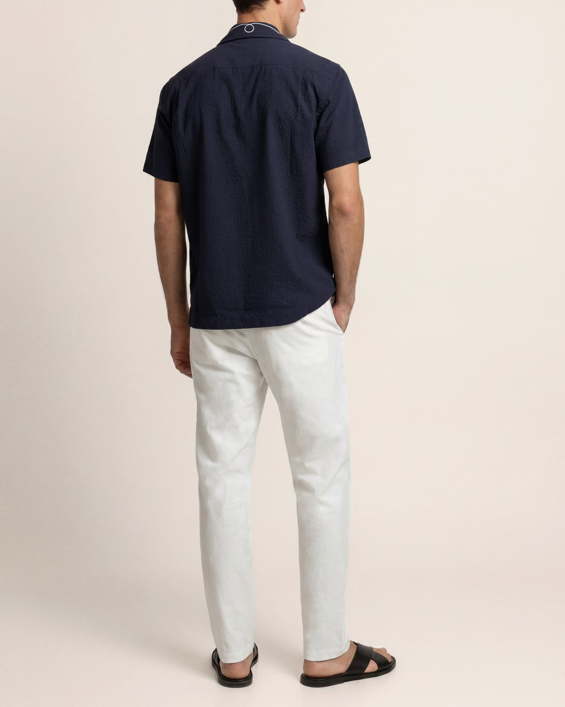 Man wearing a navy polo shirt and light-colored pants on a beige background
