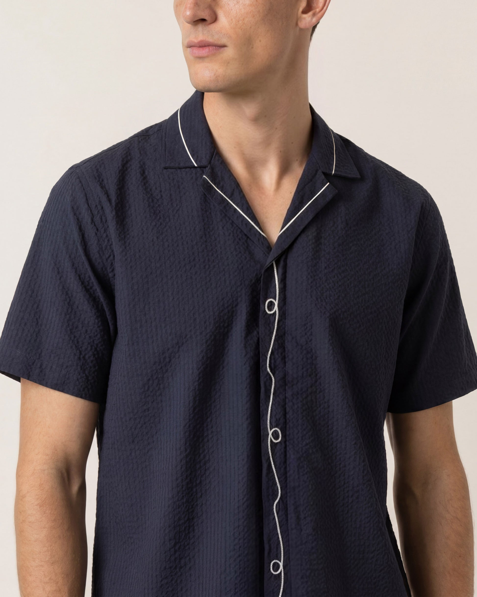 Man wearing a navy short-sleeve shirt with white trim on a neutral background