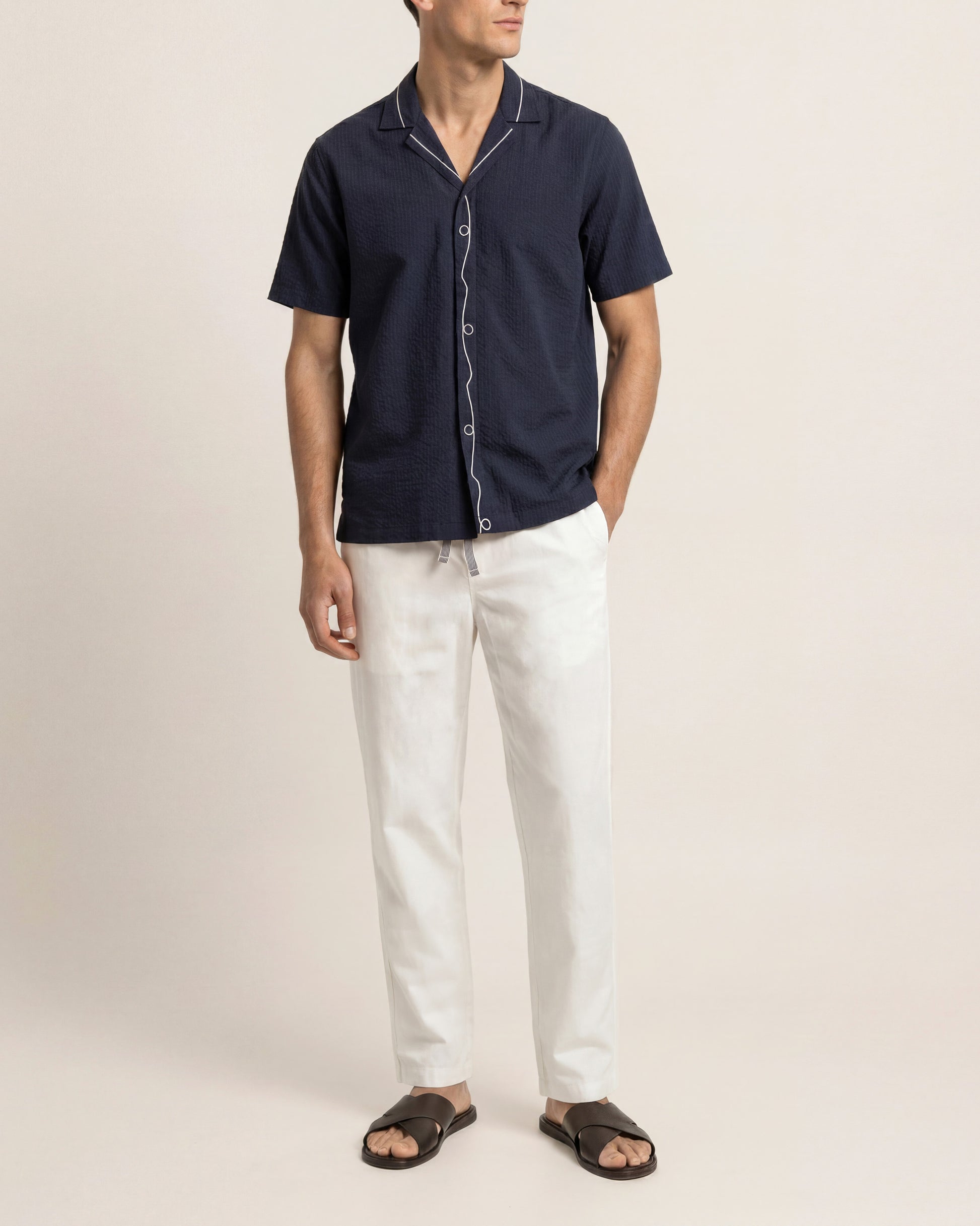 Man wearing a navy short-sleeve shirt and white pants on a beige background