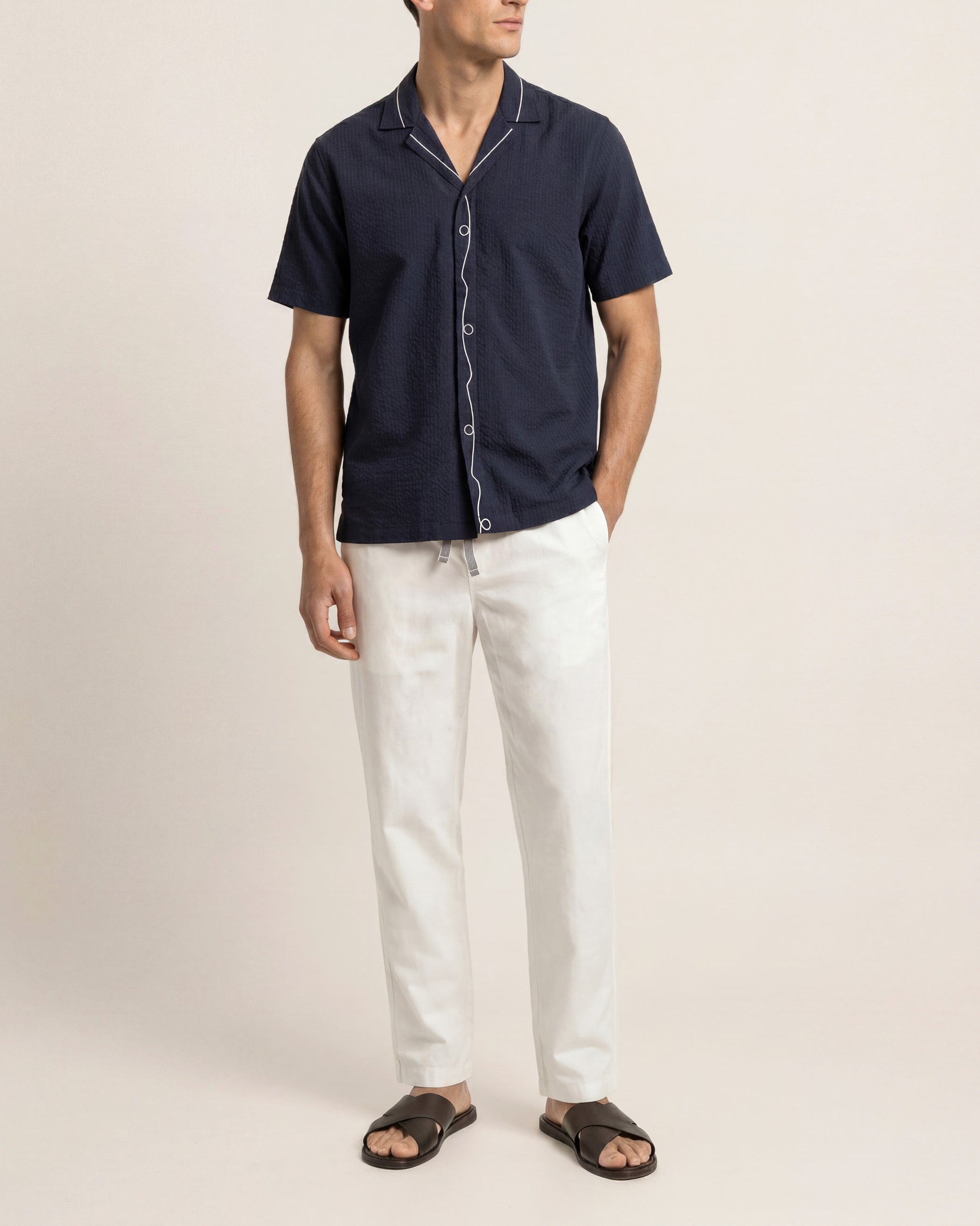 Man wearing a navy short-sleeve shirt and white pants on a beige background