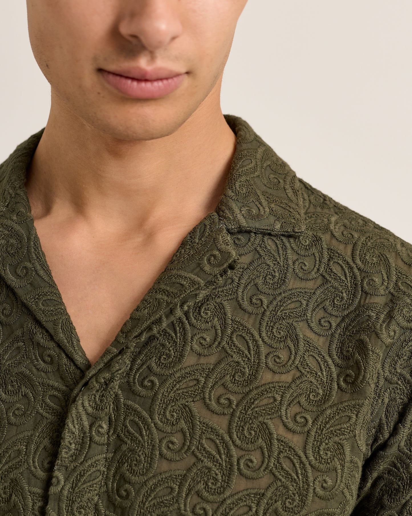 Close-up of a person wearing a green patterned garment against a neutral background