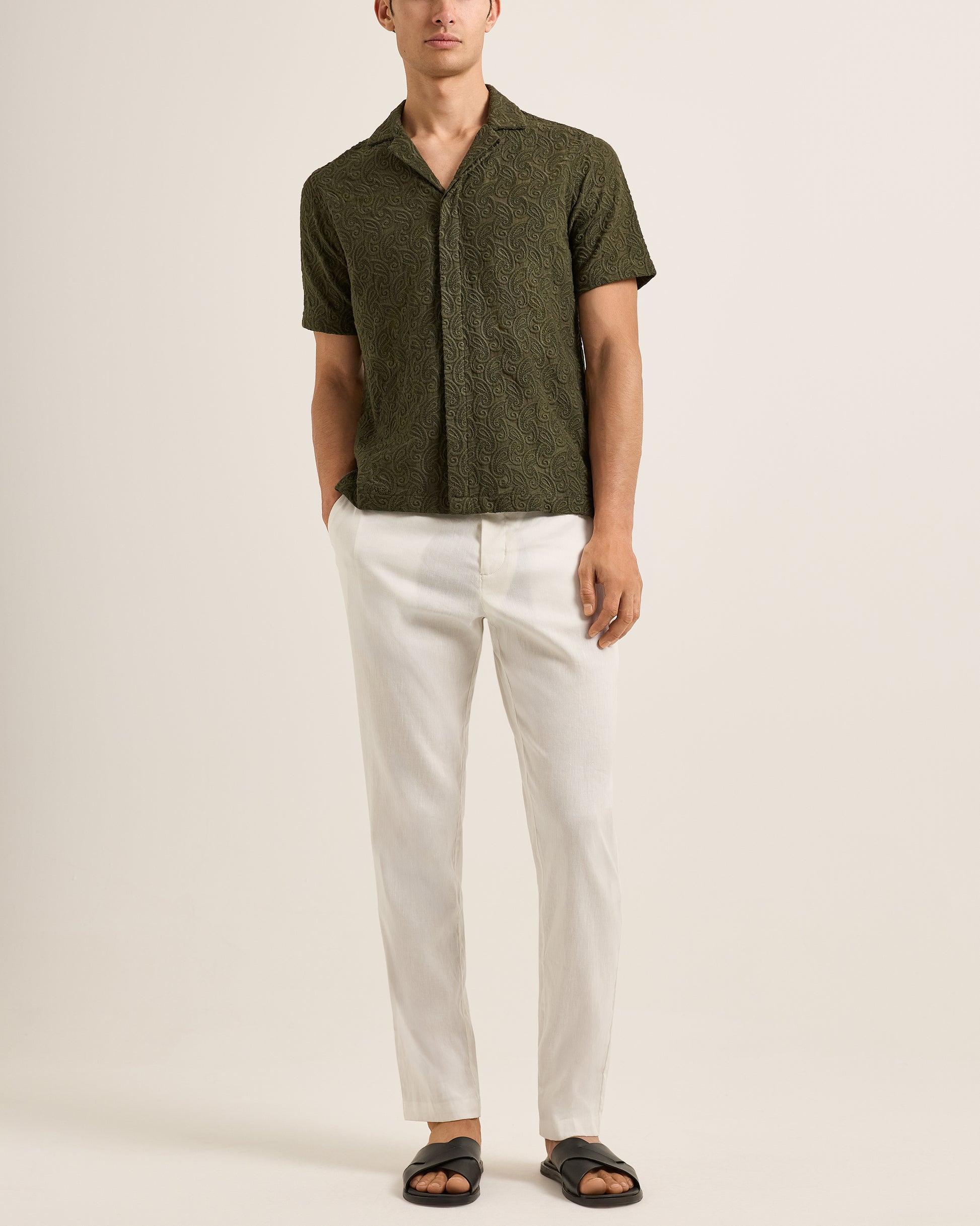 Man wearing a green patterned shirt and white pants on a plain background