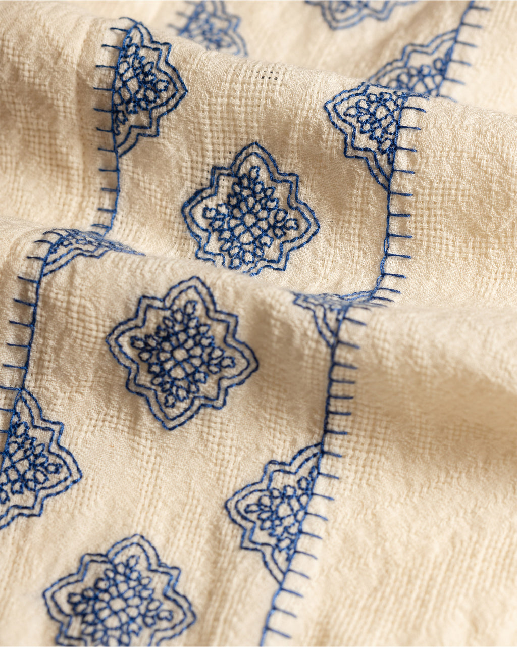 Close-up of beige fabric with blue embroidered floral patterns