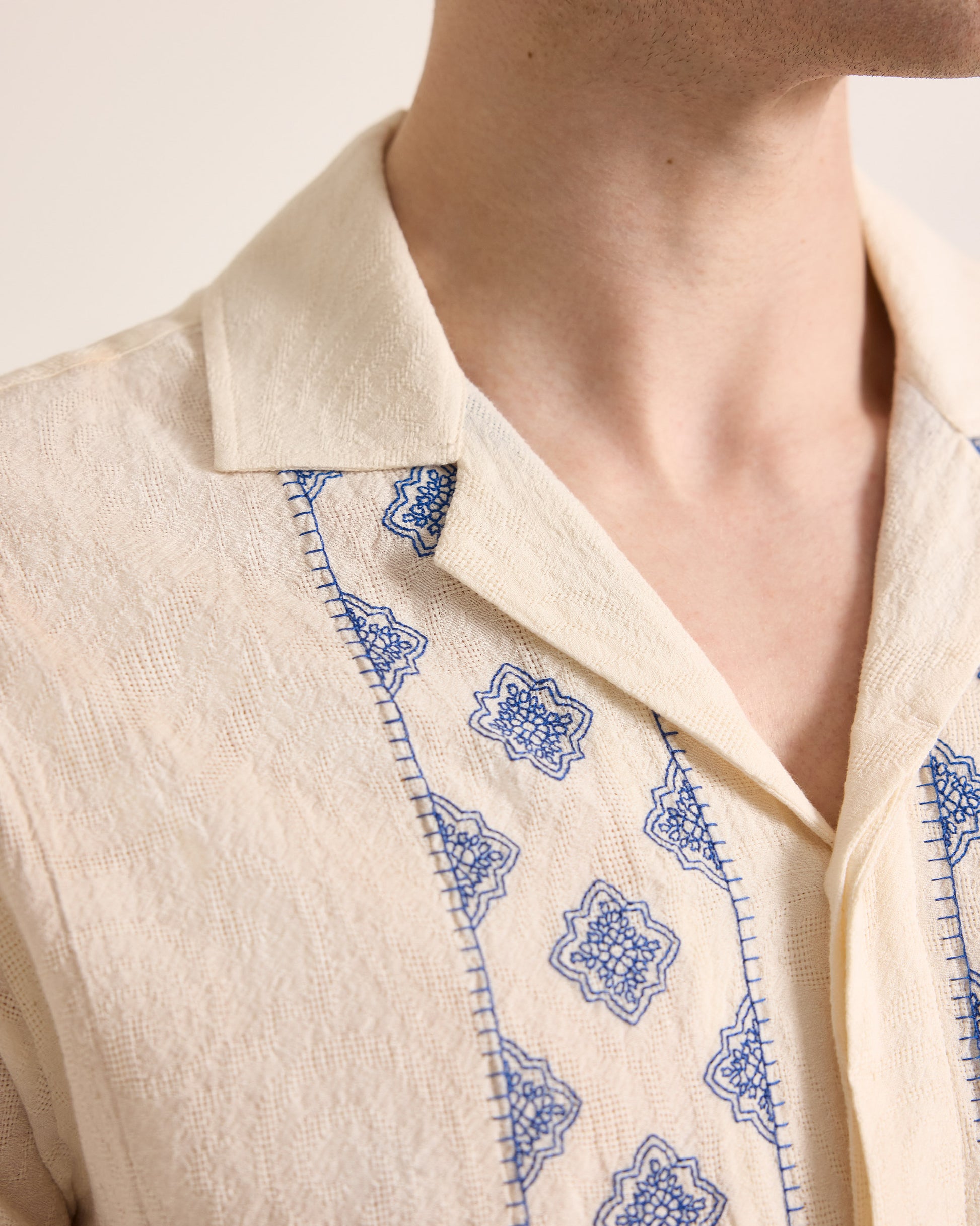 Close-up of a beige garment with blue embroidery on a neutral background