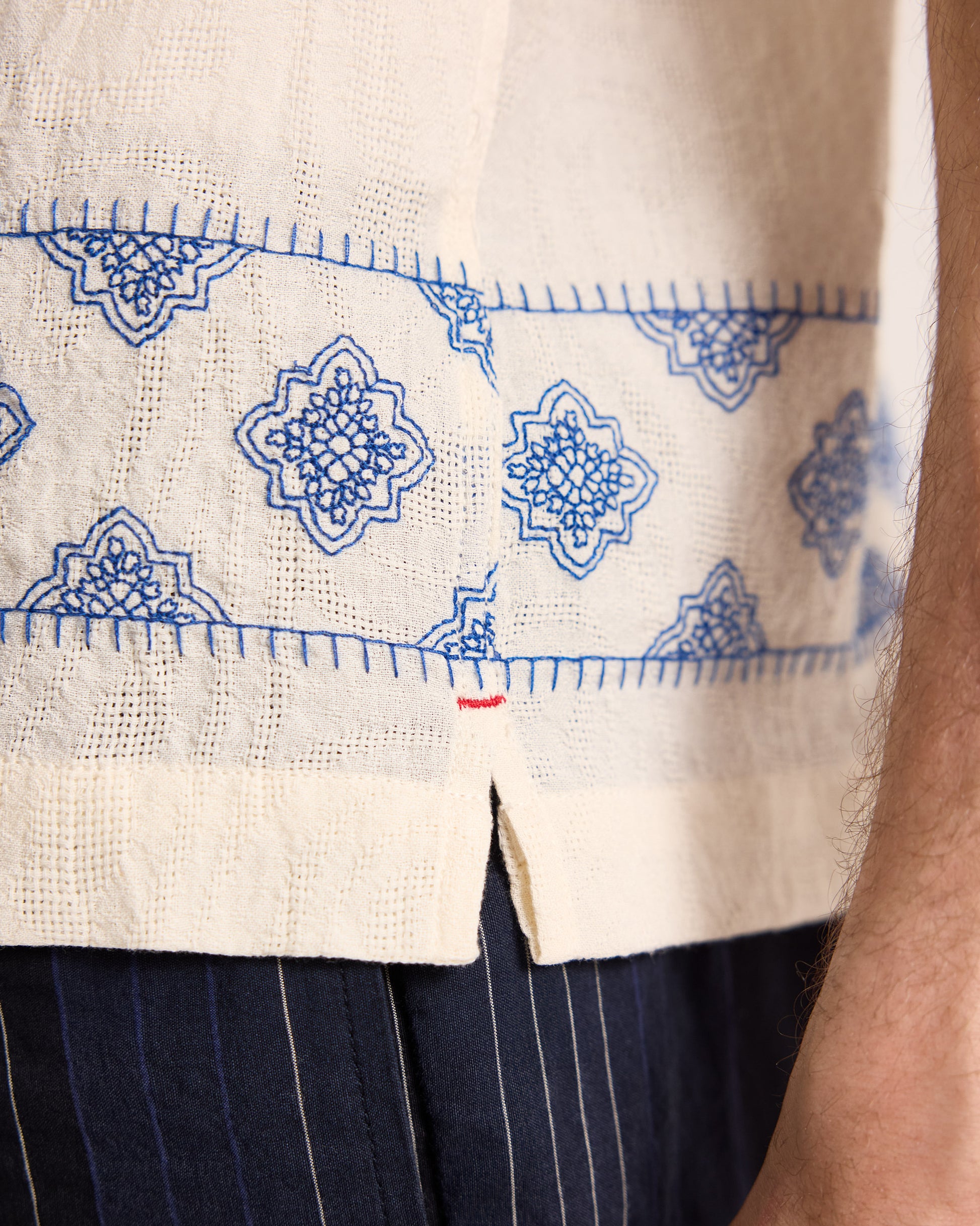 Close-up of a white garment with blue embroidery and dark pants.