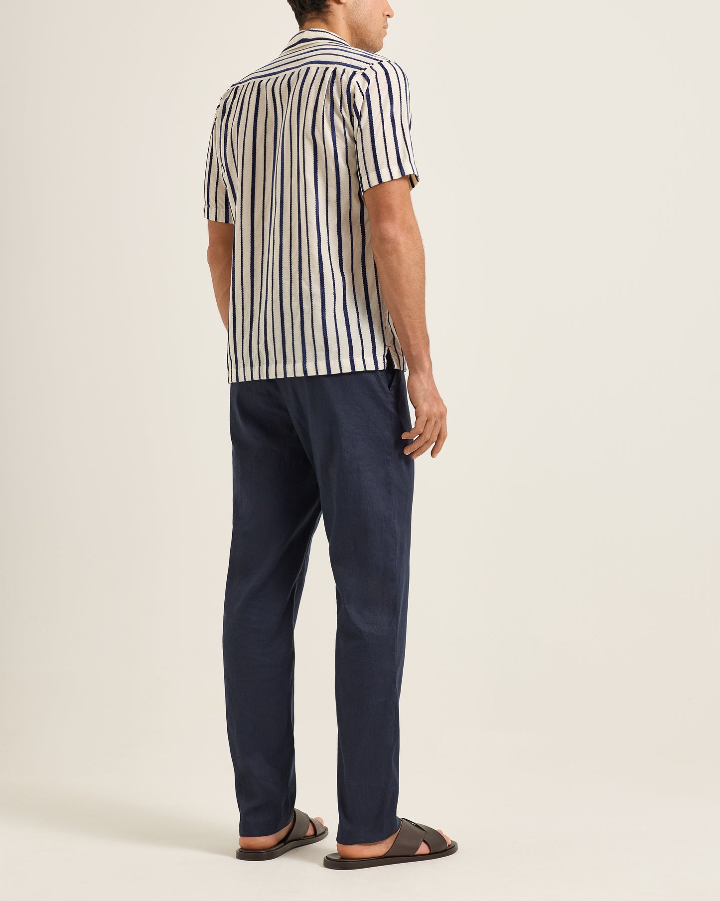 Person wearing a striped shirt and navy pants on a plain background