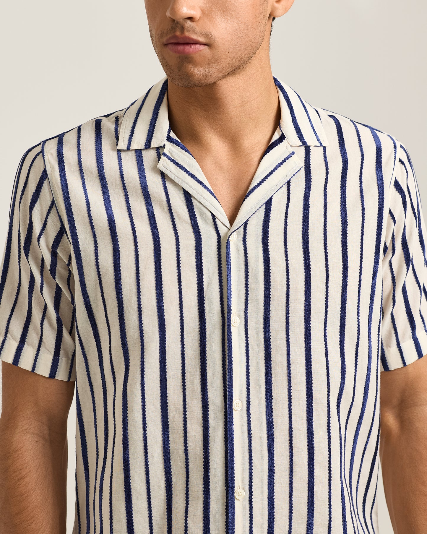 Man wearing a blue and white striped shirt against a neutral background